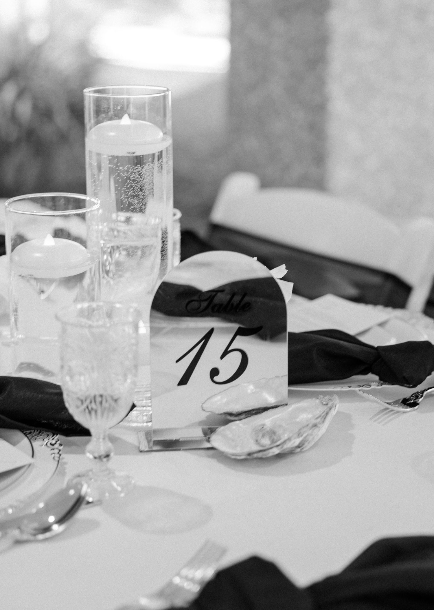 Black and white photo of wedding reception table number 15 with elegant candles, glassware, and black bow tie napkins.