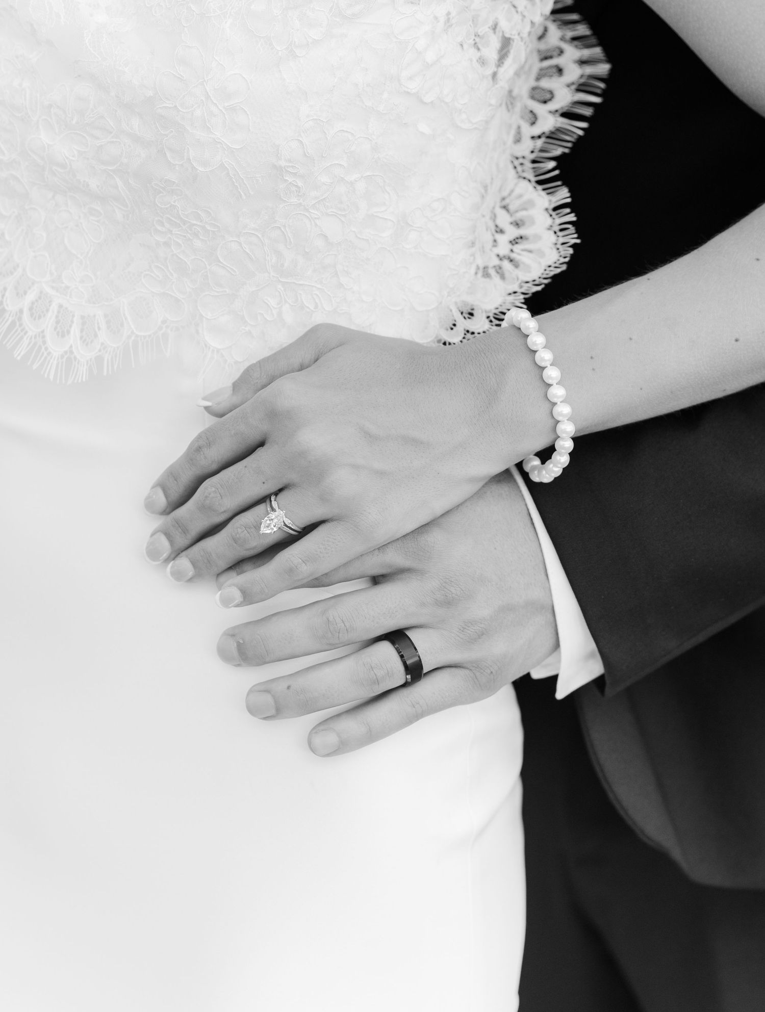 Black and white photo of newlyweds hands showing wedding rings and pearl bracelet.