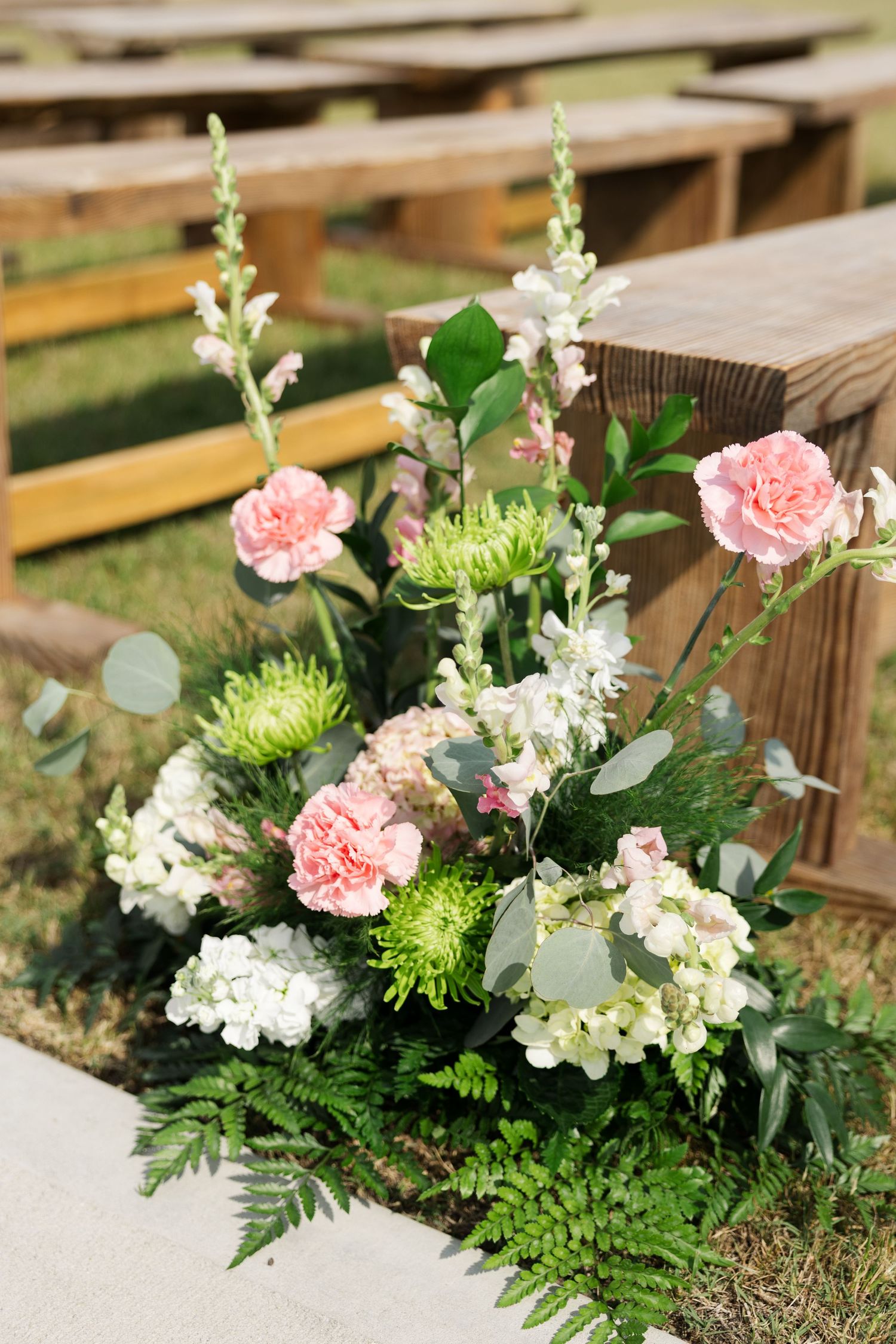Outdoor wedding ceremony aisle floral arrangement with pink carnations, white hydrangeas, and green chrysanthemums.