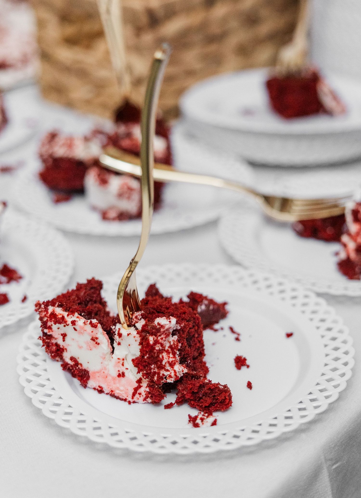 Partially eaten red velvet cake slice on white doily plate with gold fork at wedding reception.