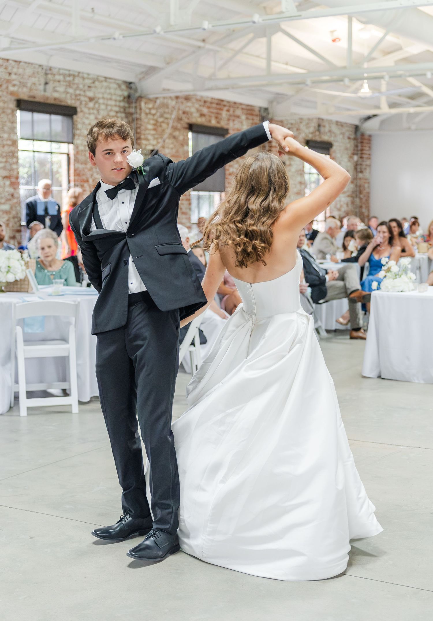 Bride and groom share first dance, groom spinning bride in white ballgown at wedding reception.