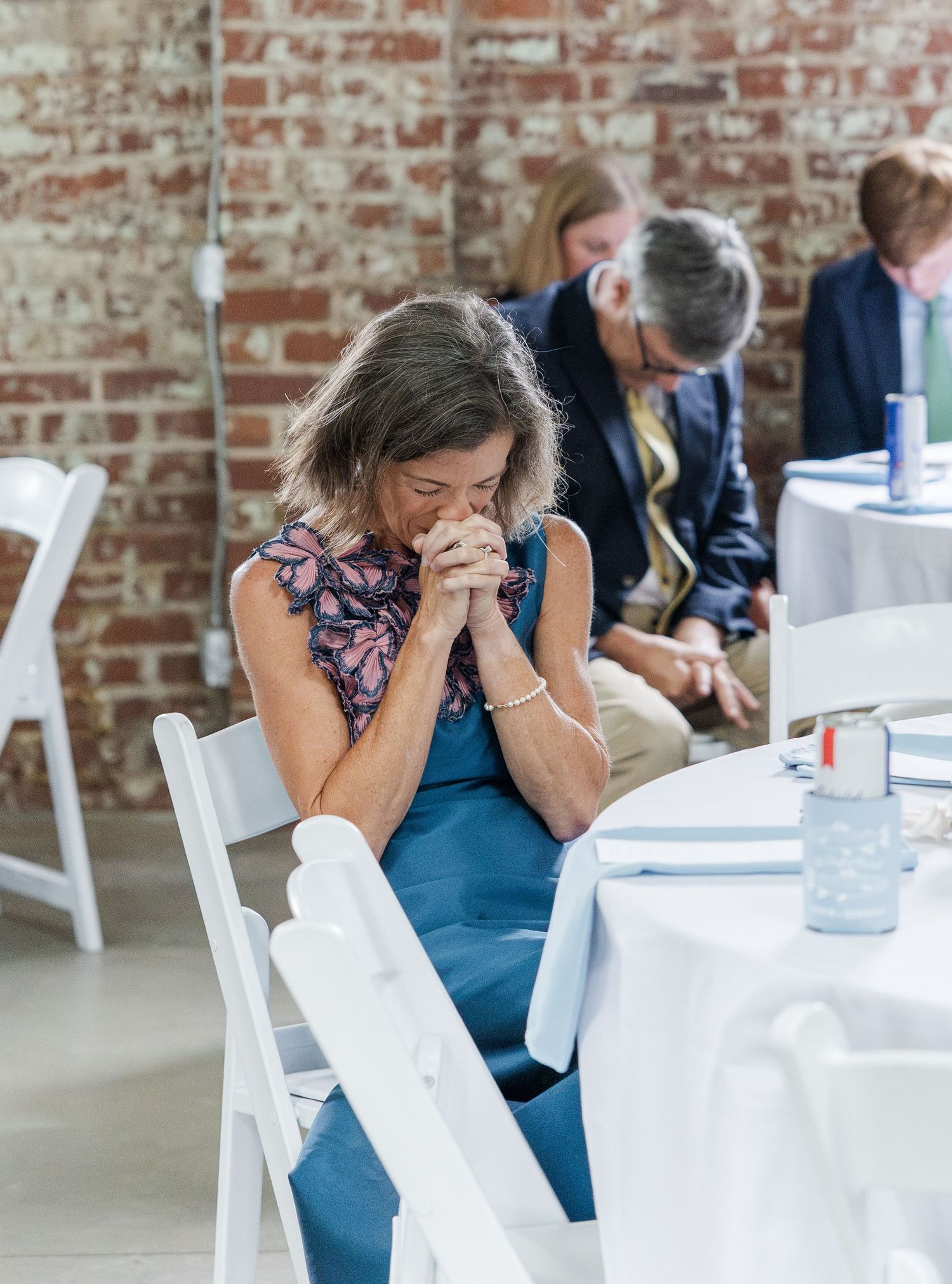 Emotional wedding guest bows head in prayer during wedding reception blessing.