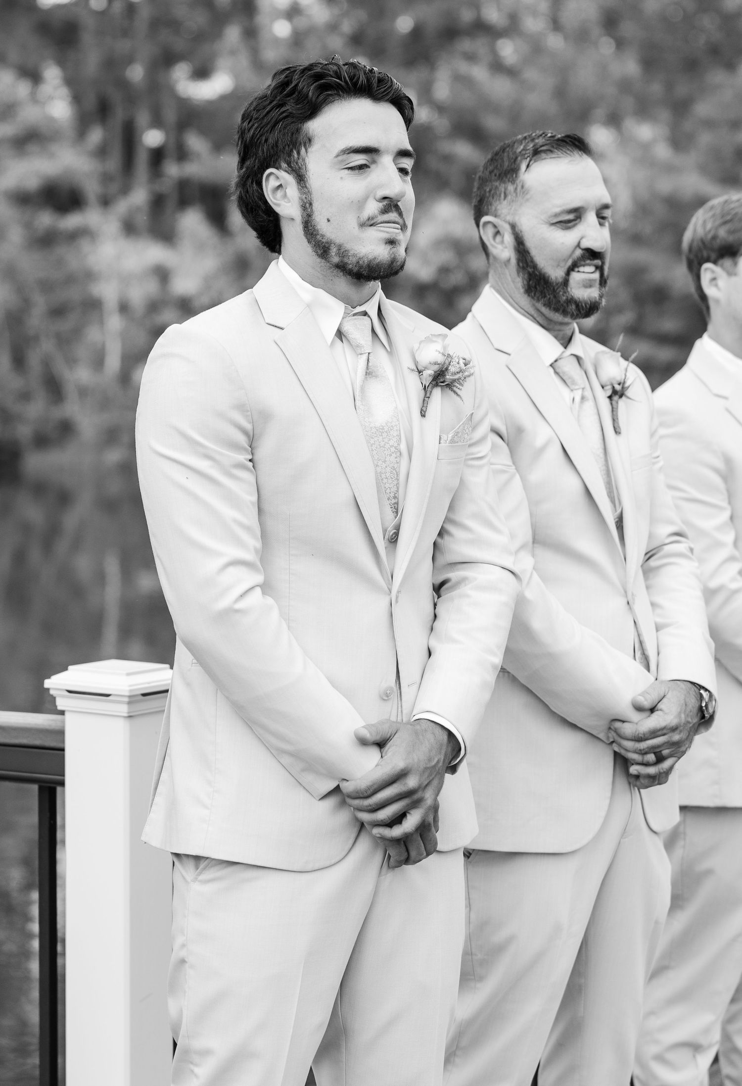 Black and white photo of groom in light suit with boutonniere standing at wedding altar with groomsmen.