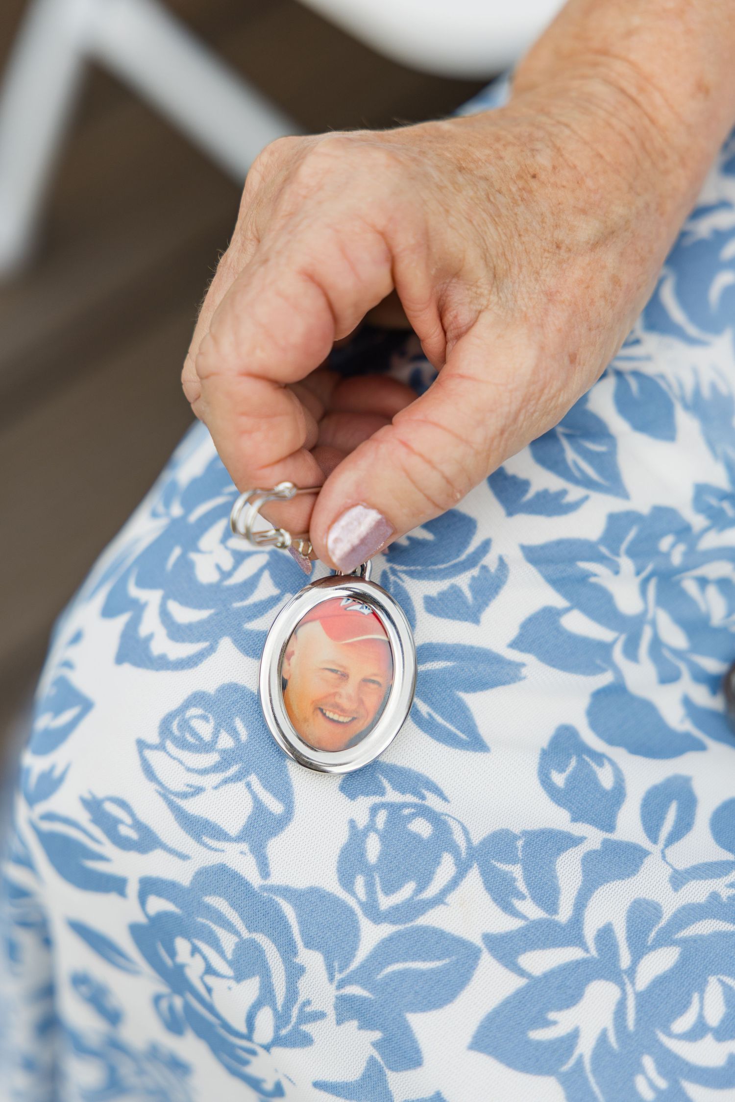 Elderly woman holding silver oval locket with photo of loved one in blue floral dress.