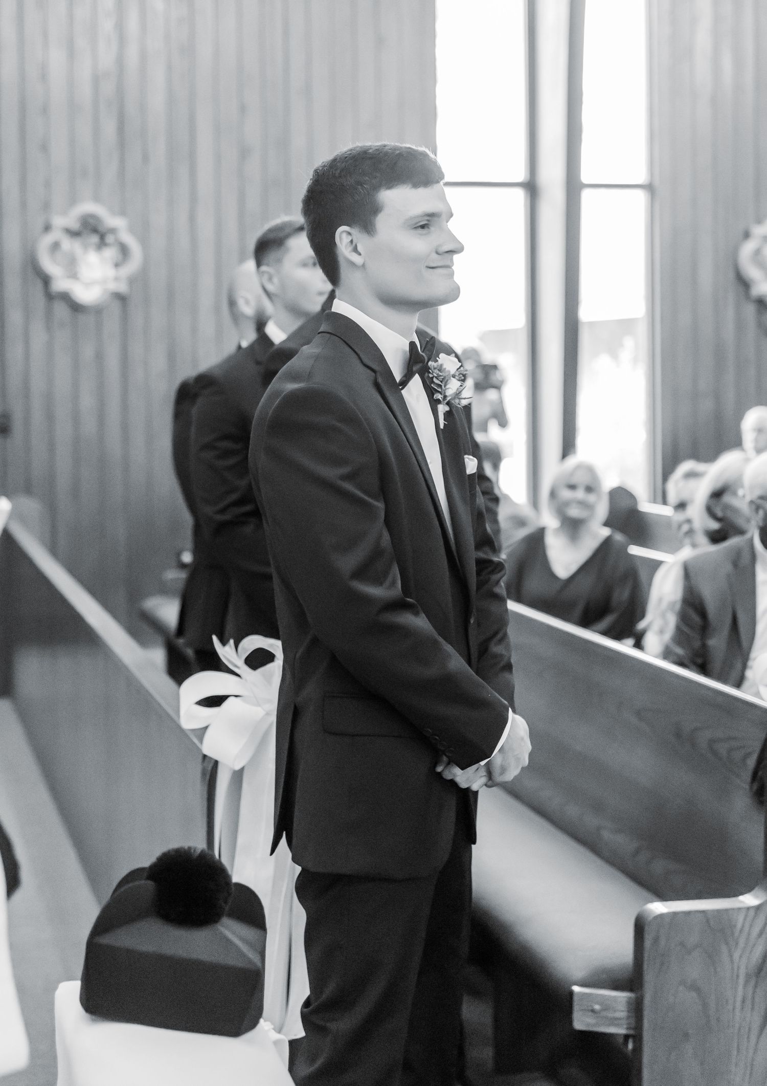 Black and white photo of groom waiting at church altar with pews in background.