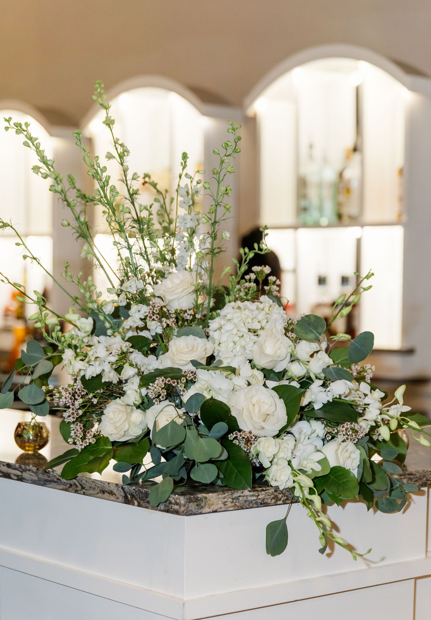Elegant white floral wedding arrangement with roses, hydrangeas, and eucalyptus greenery displayed on a white altar.