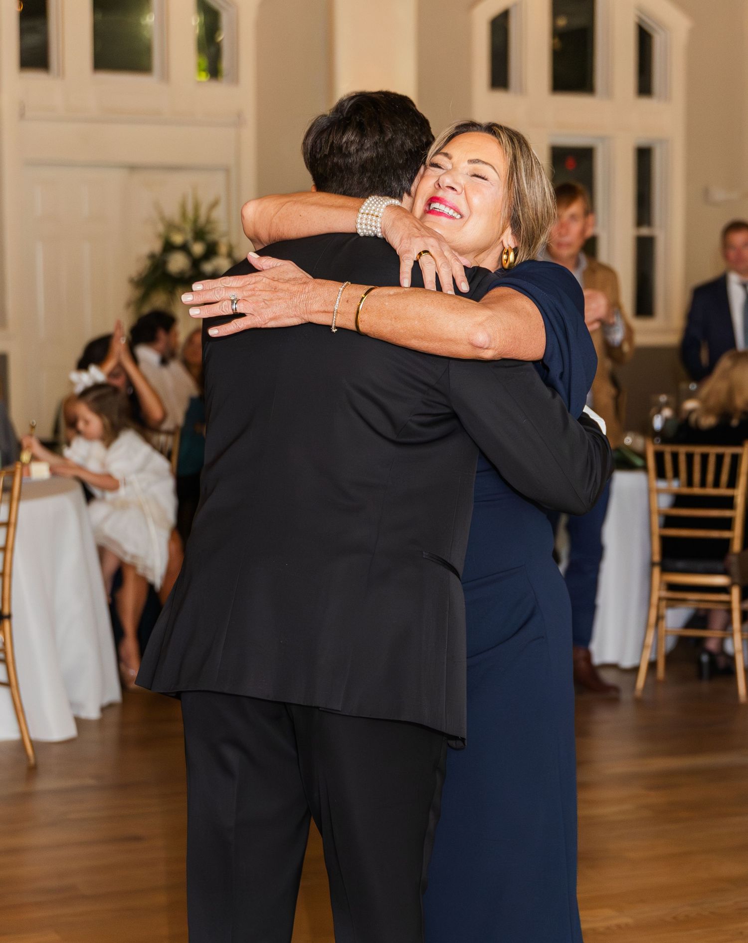 Mother and son share a warm embrace during wedding reception dance on hardwood floor.