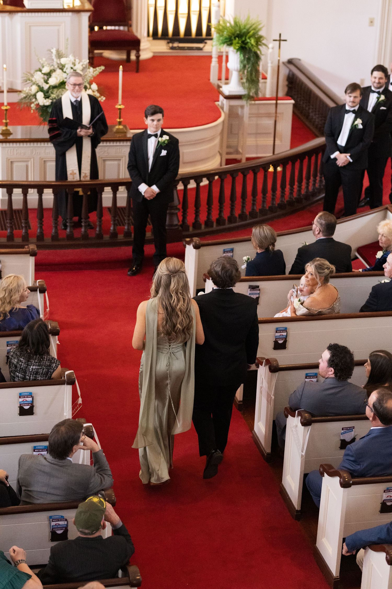 Wedding ceremony in a classic church with groom at altar as guests watch a woman escorted down the aisle.