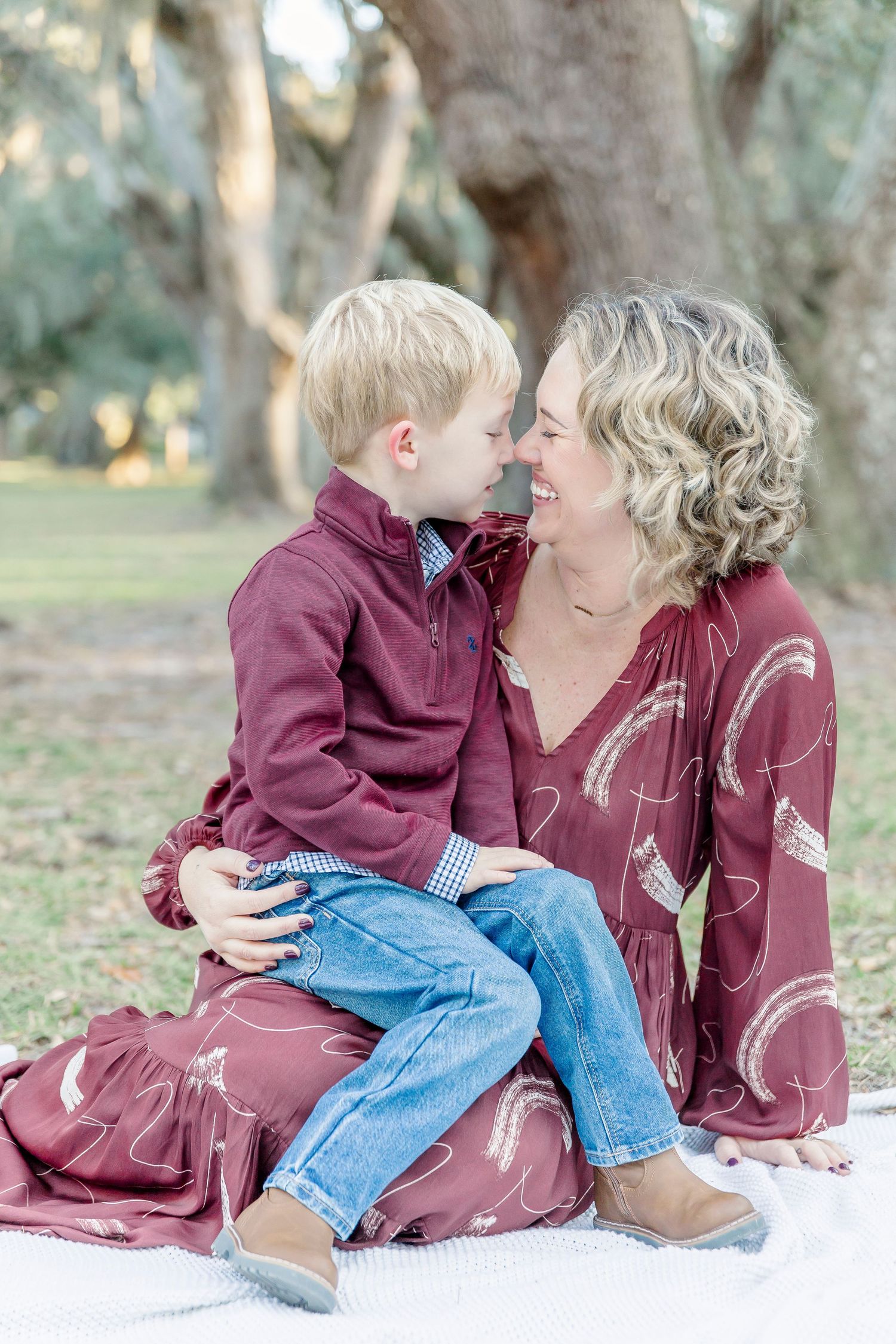 A heartwarming moment between parent and child sitting on a blanket under oak trees.
