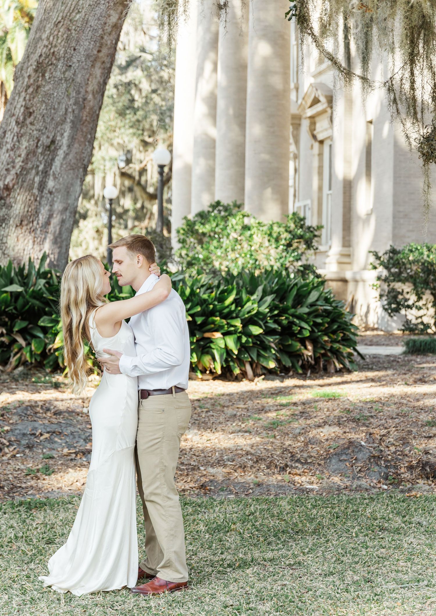 Newlyweds share romantic moment in garden setting with classic columns and Spanish moss.