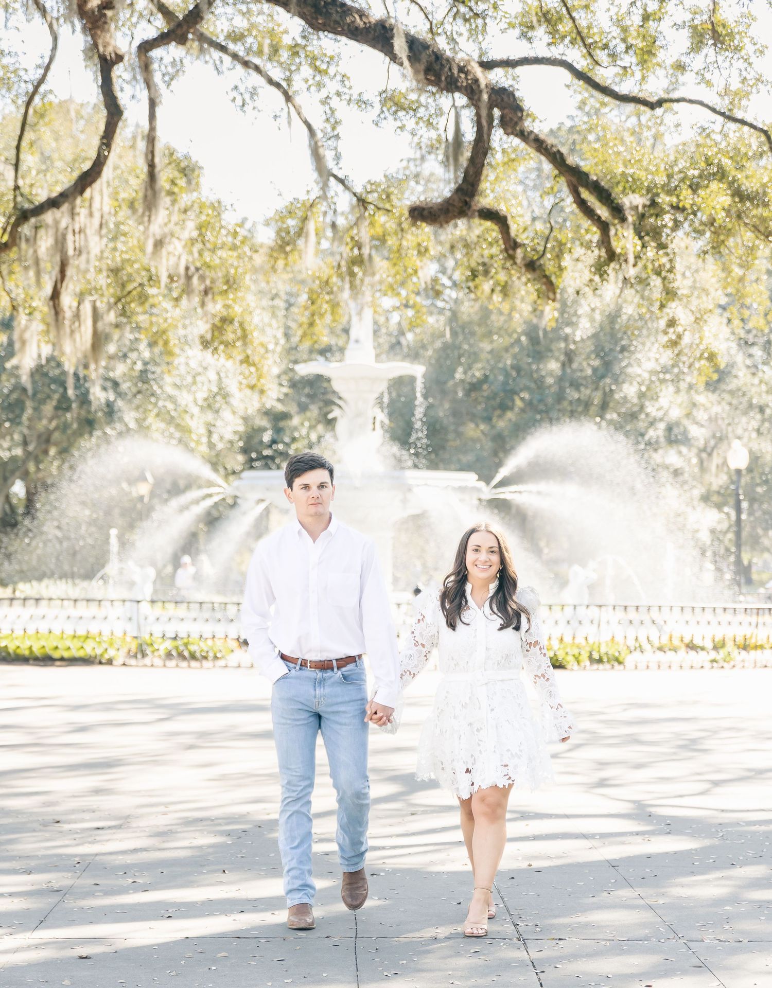 Couple strolling hand in hand by ornate fountain in a scenic garden with Spanish moss.