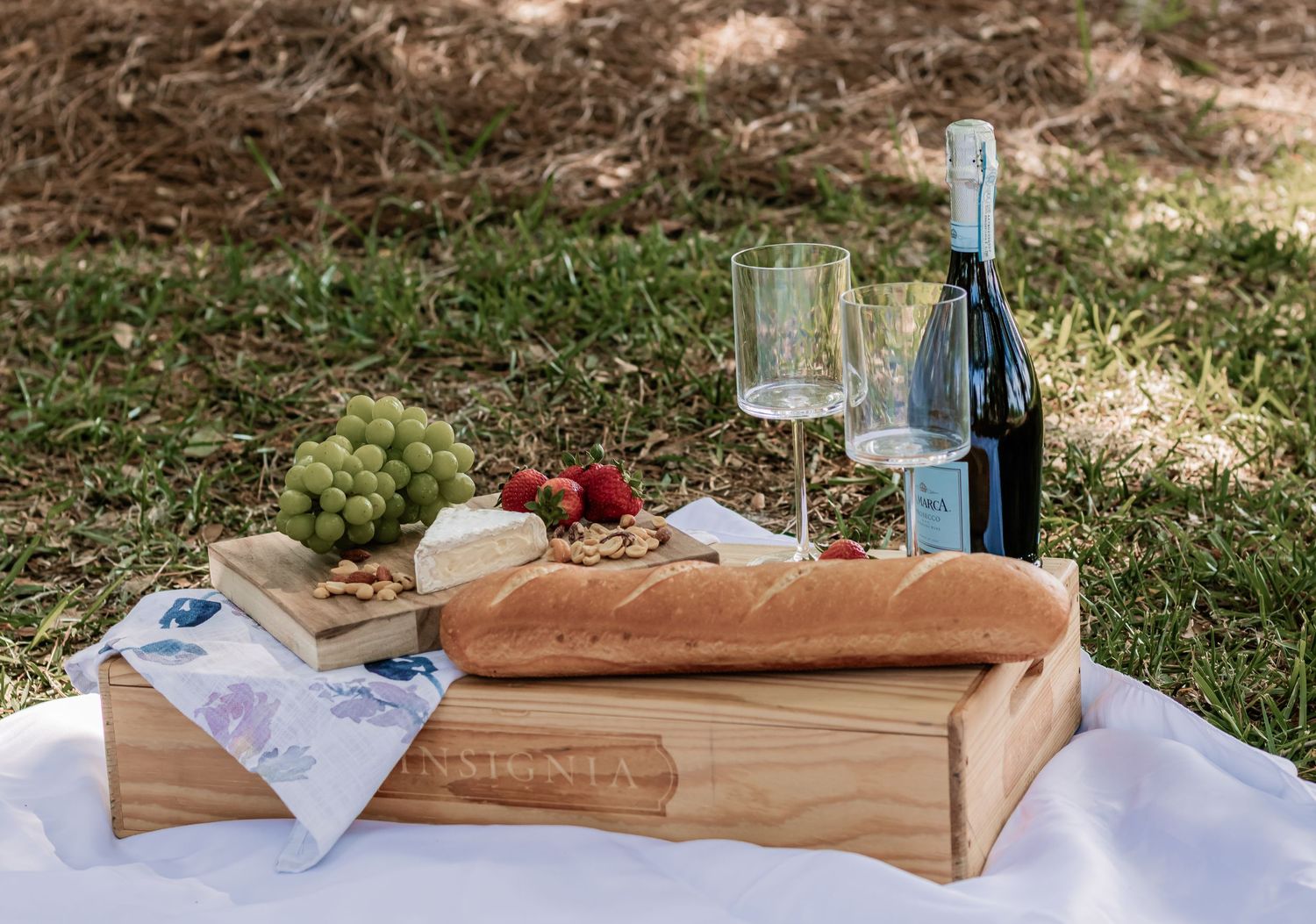Wine bottle, baguette, and snacks artfully arranged on wooden serving board for outdoor picnic.