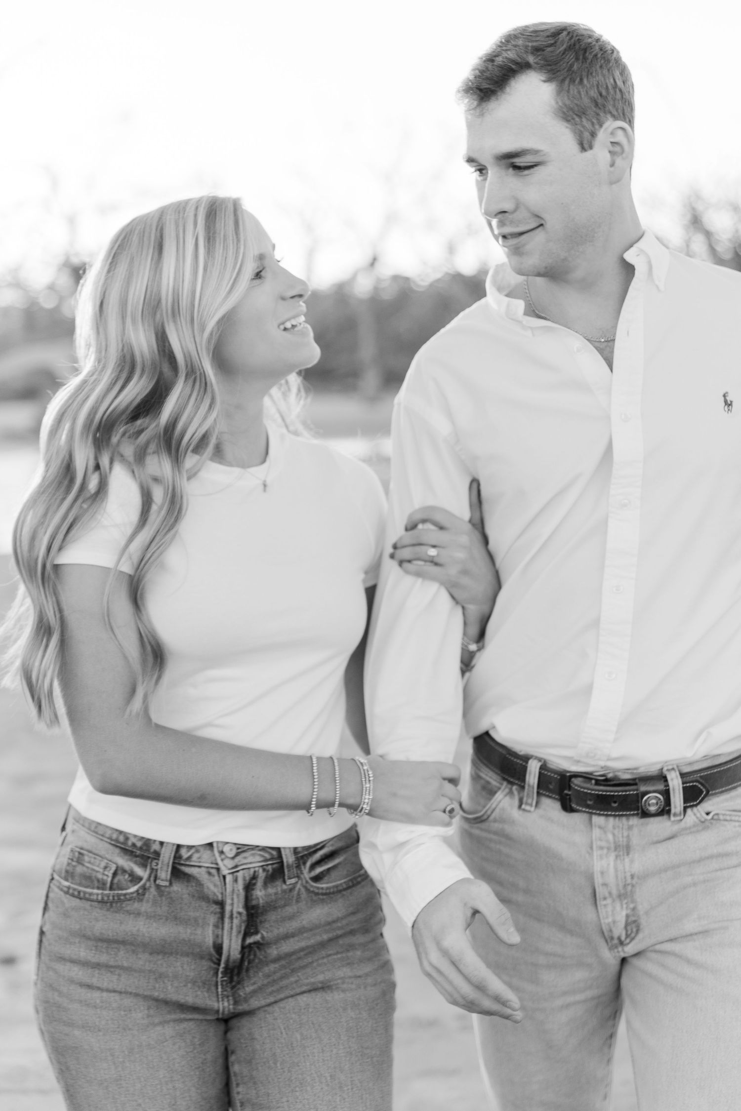 A couple in matching white shirts and jeans smiles at each other in black and white.