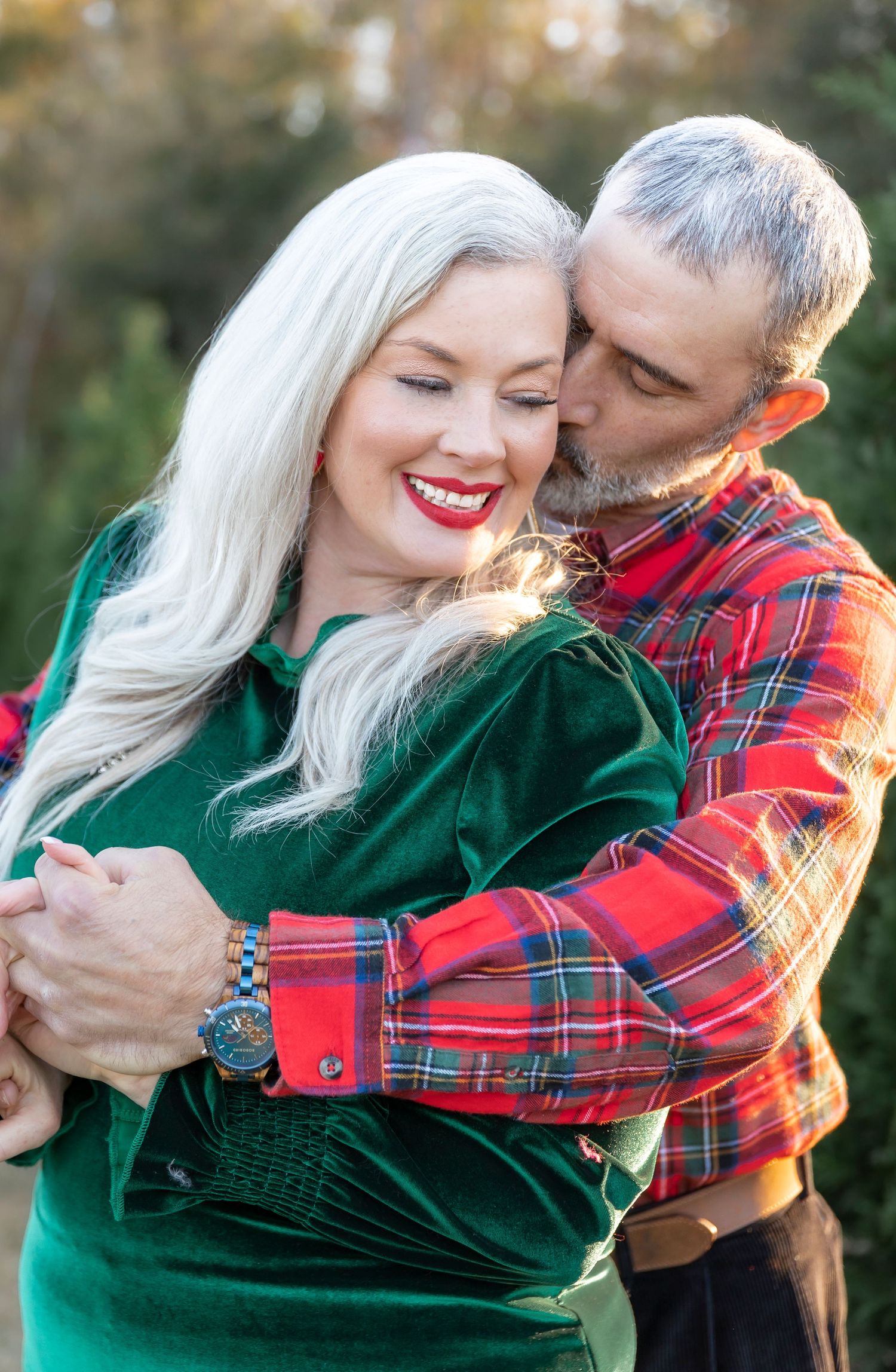 Tender embrace between couple wearing coordinating holiday outfits of plaid and velvet.
