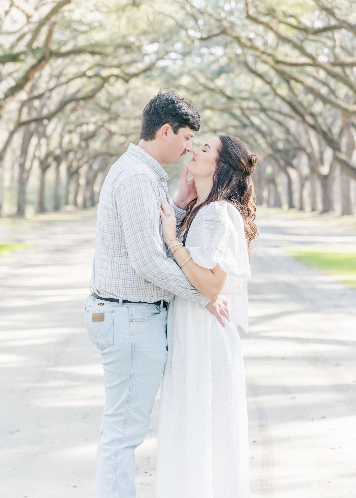 An intimate embrace shared between a couple beneath an archway of oak trees.