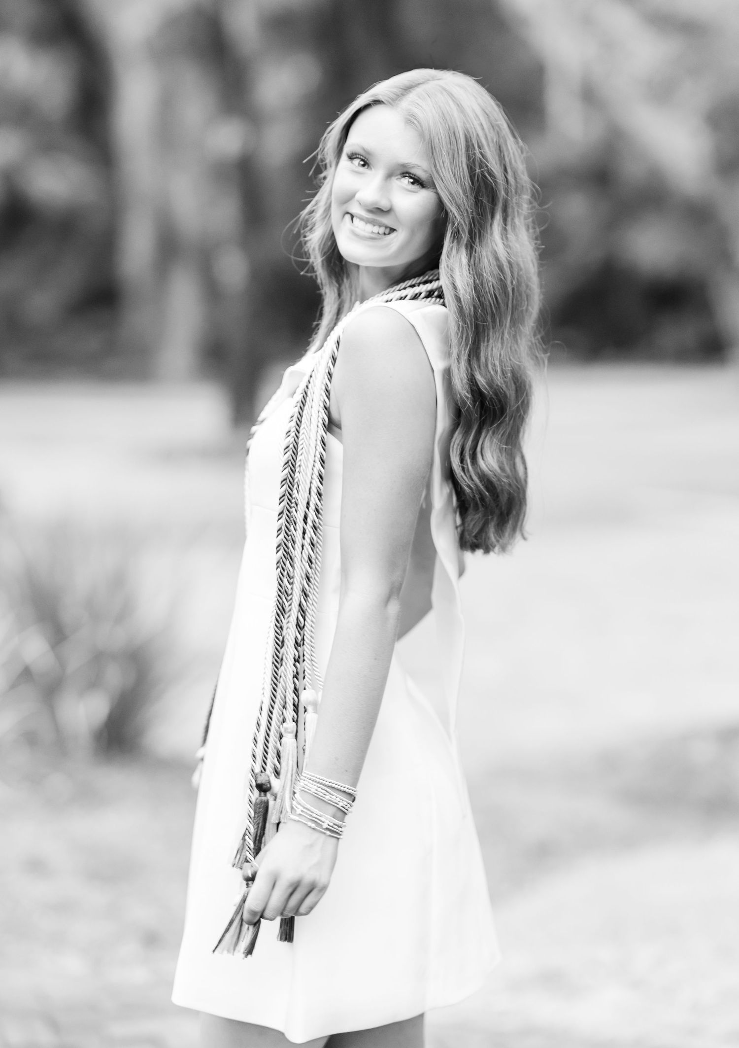 Black and white portrait of a person in a white dress with long wavy hair looking over their shoulder with a bright smile.