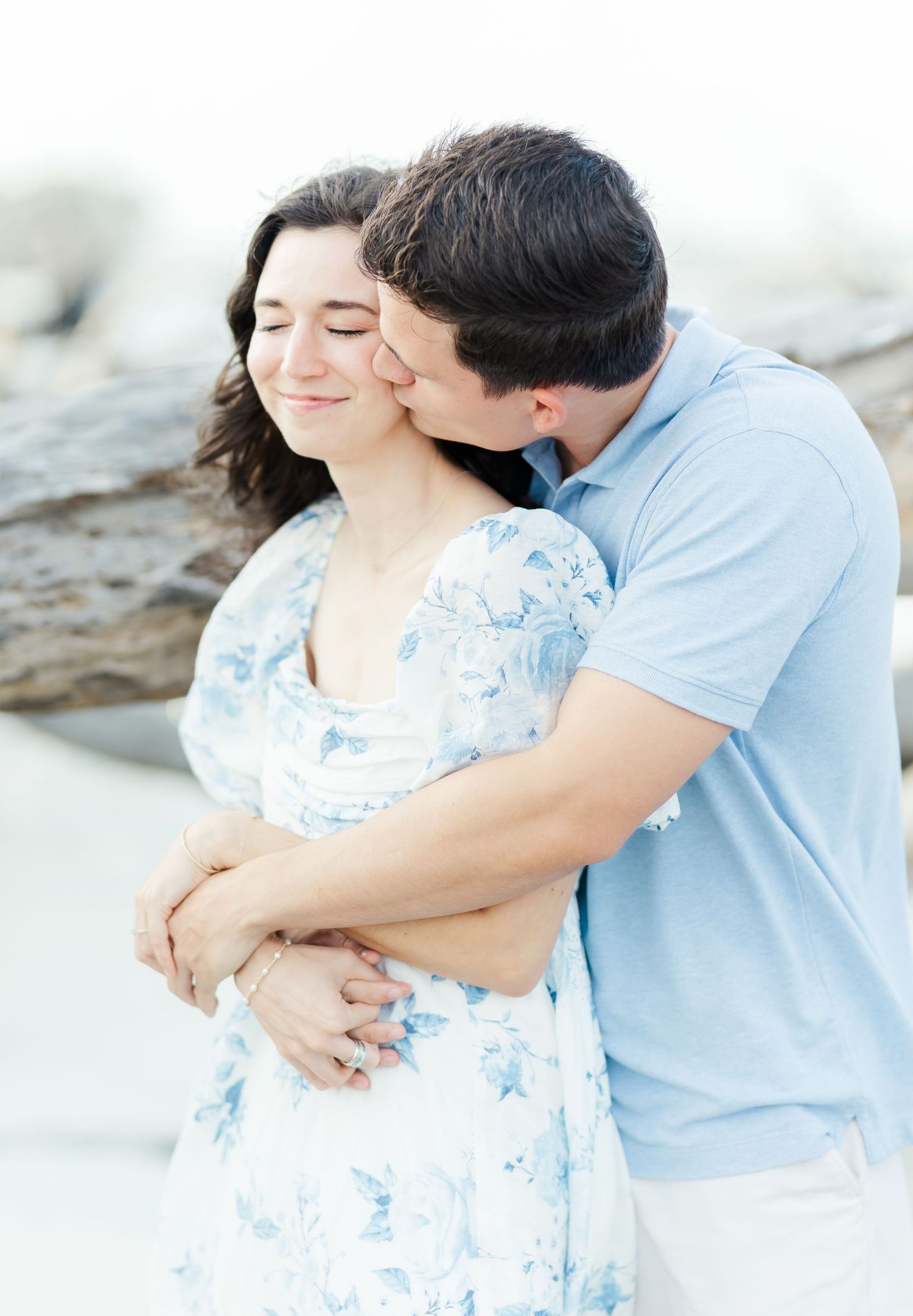 Romantic beach photoshoot of couple in coordinating blue and white outfits sharing tender moments.