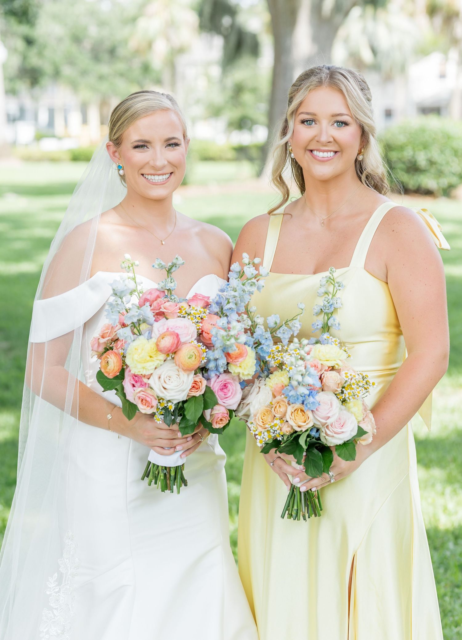 Bride in white gown and bridesmaid in yellow dress holding vibrant spring bouquets.