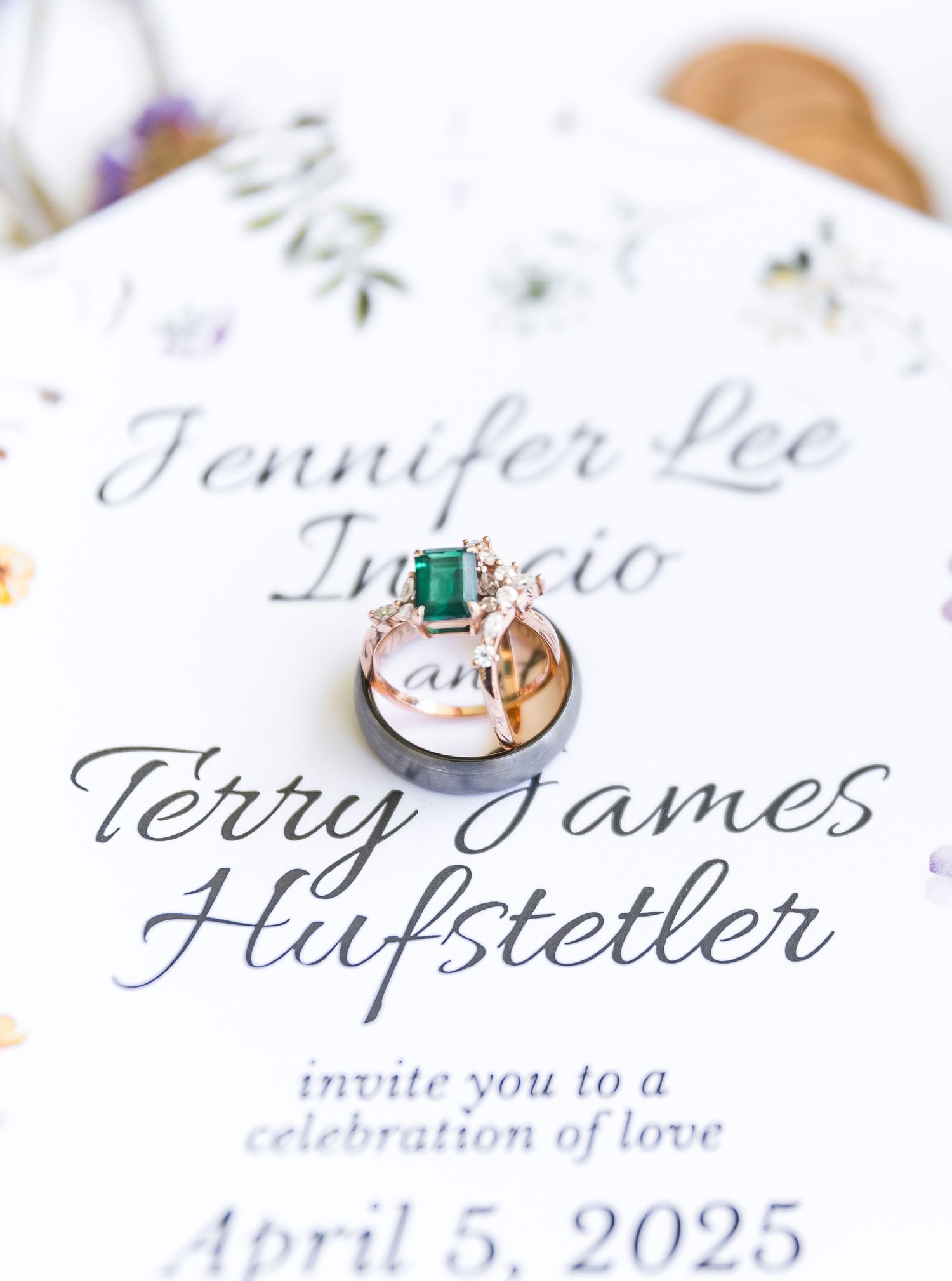 Wedding invitation with elegant calligraphy and emerald engagement ring displayed on white paper.