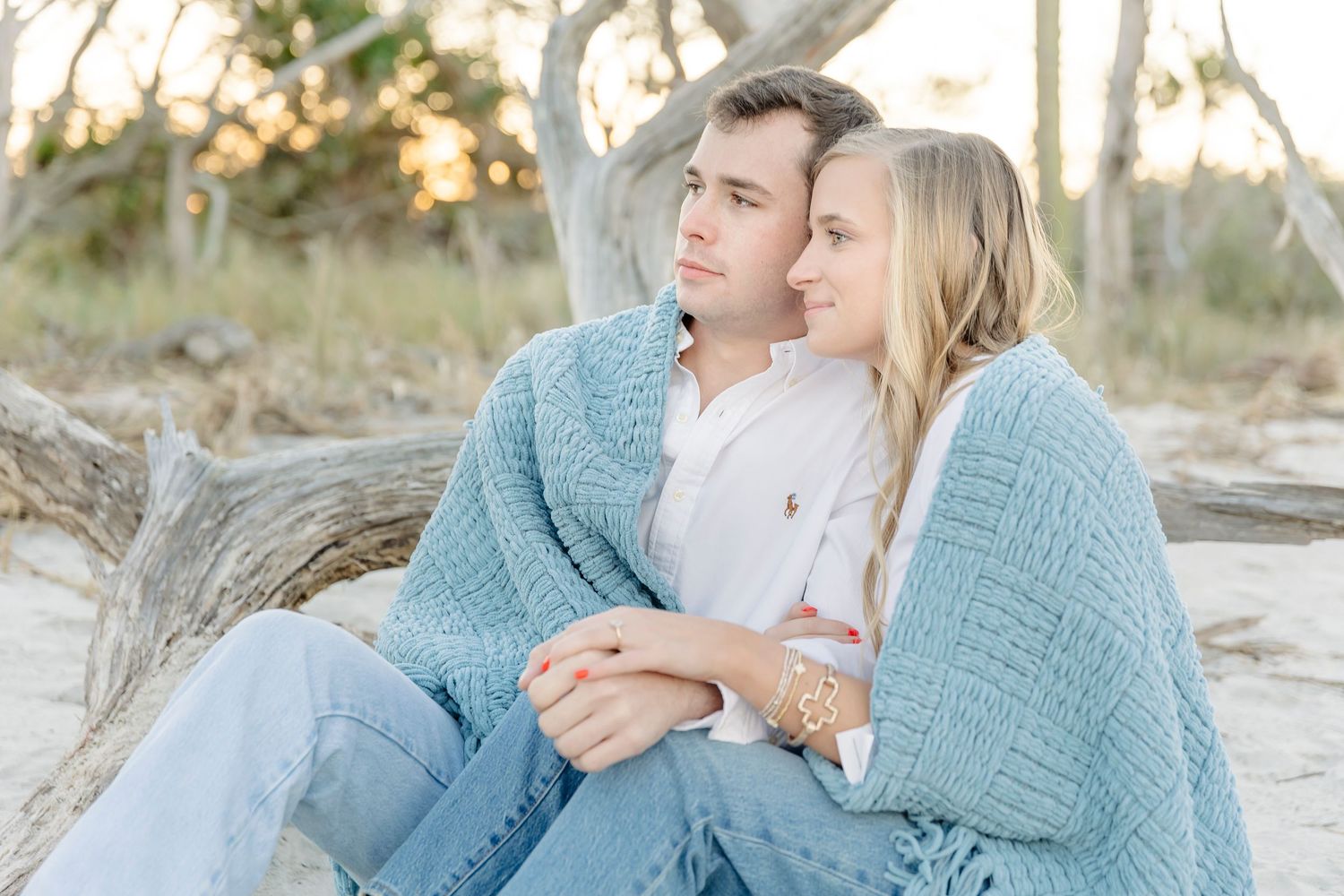 Family wearing blue and white outfits sits together on beach during sunset photo session.