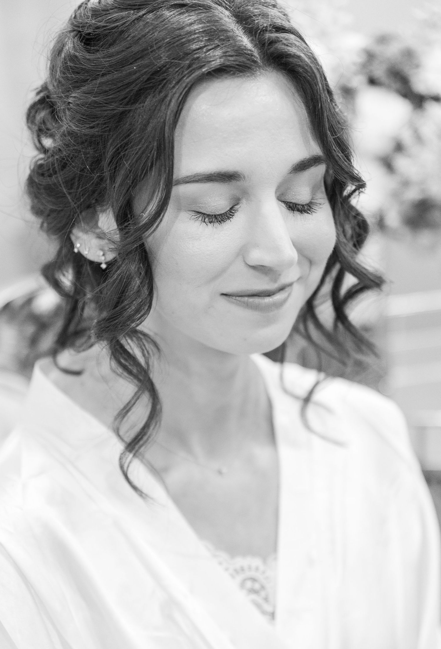 Black and white portrait of a bride with curled hair and closed eyes wearing a white robe.