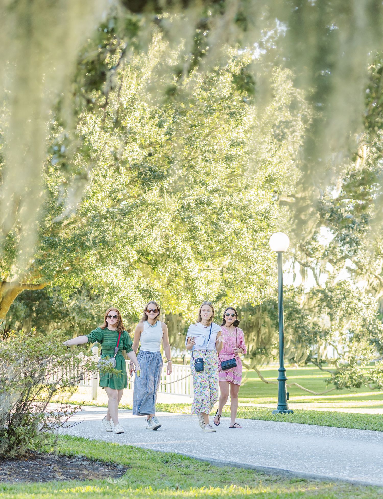 People walking along a scenic tree-lined path in a park on a bright sunny day.