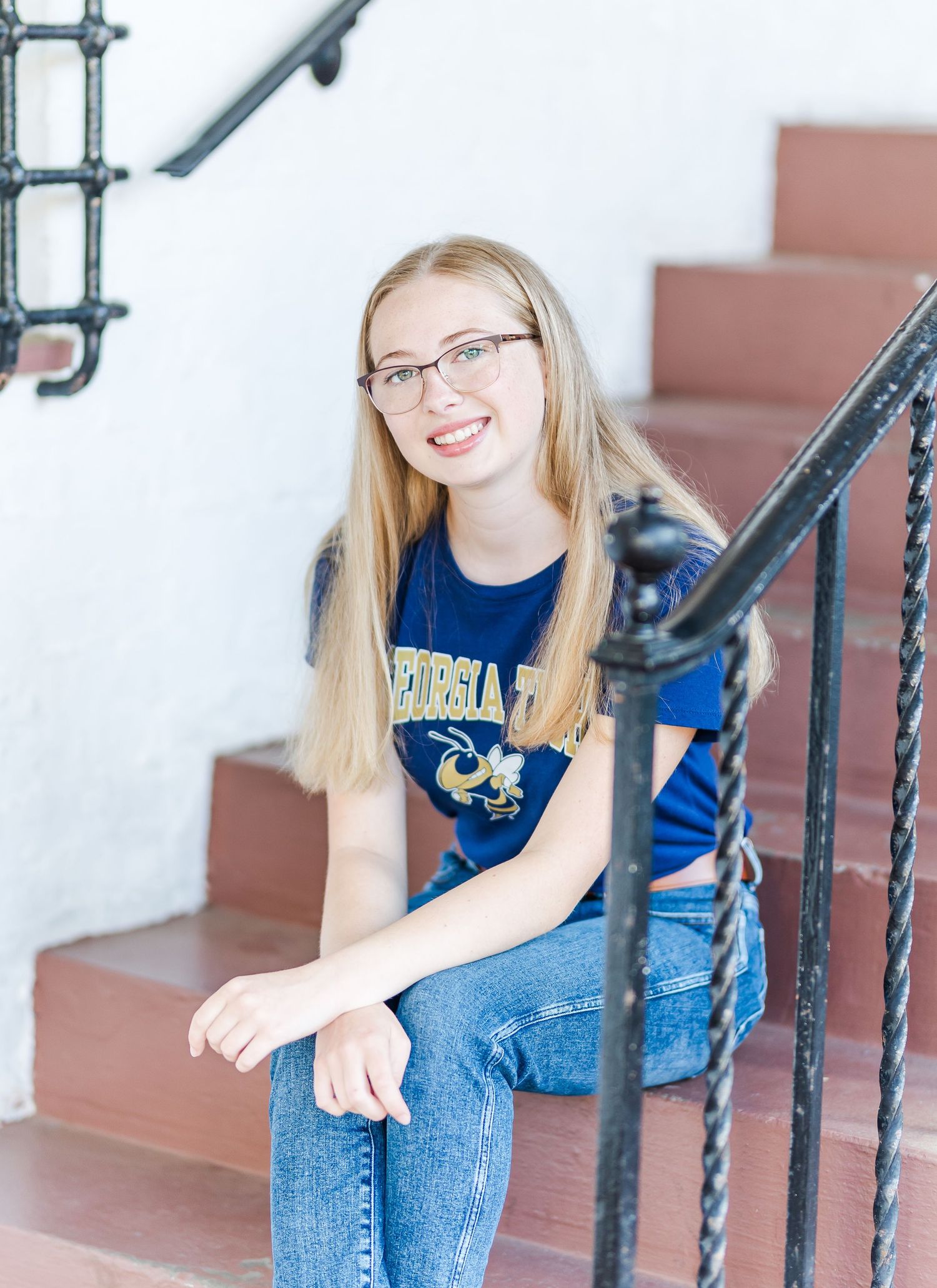 Person sits on stairs with iron railing wearing university t-shirt and jeans.