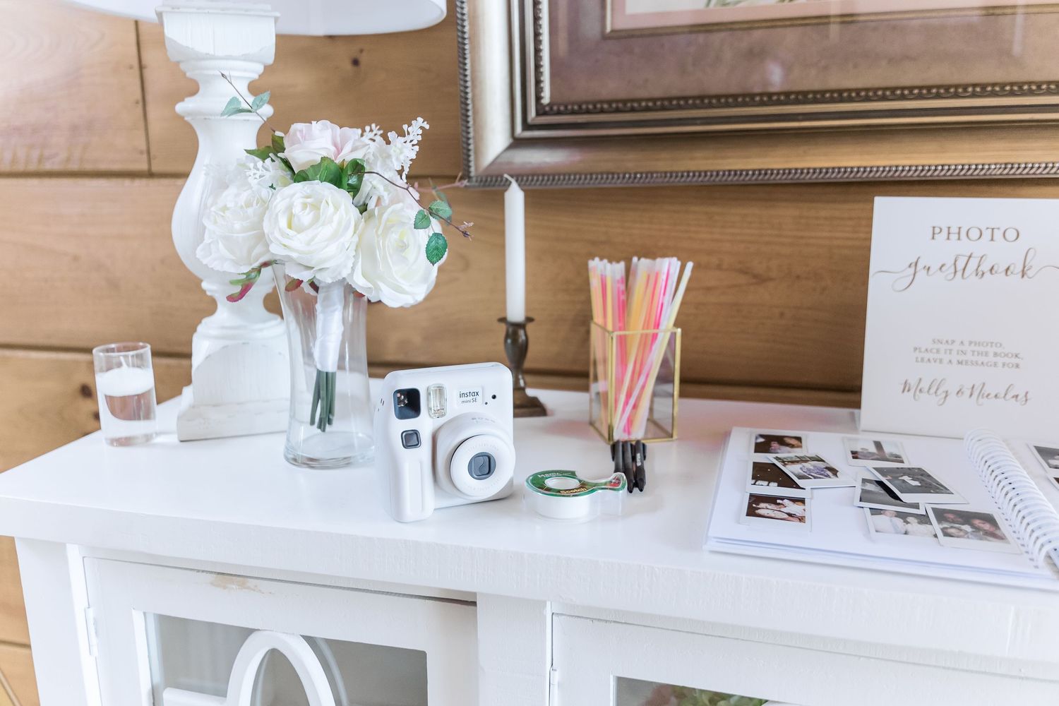 Wedding photo guestbook setup with instant camera, flowers and white decor on table.