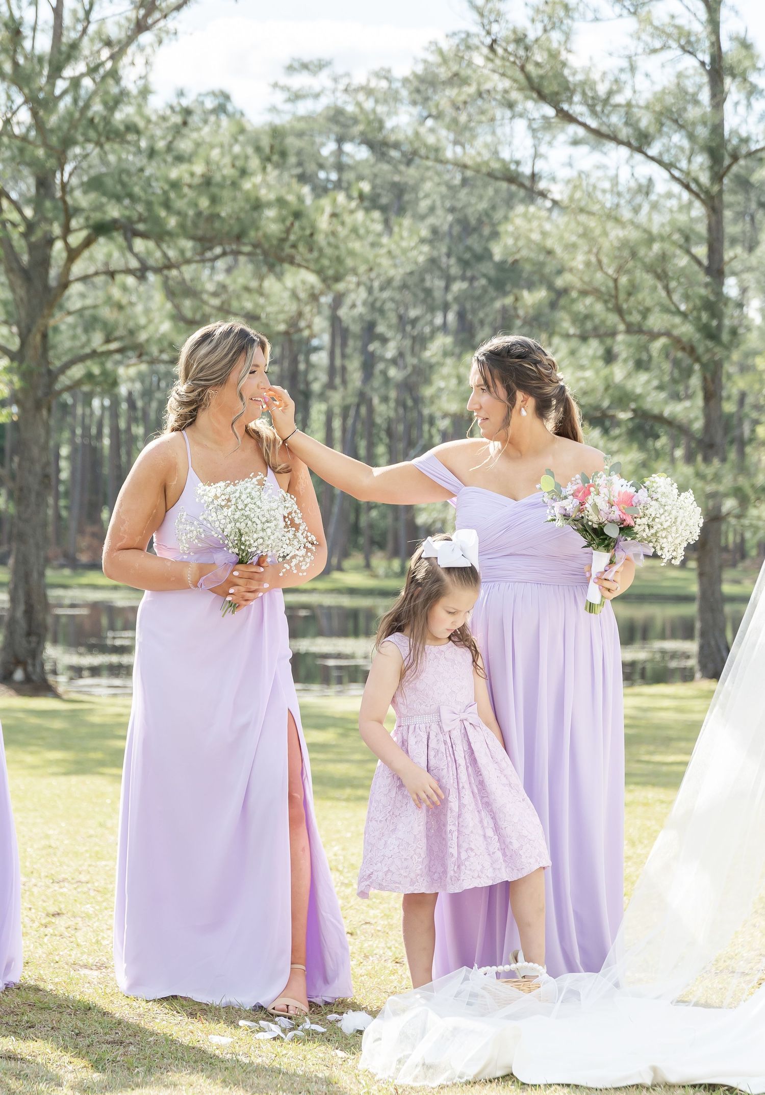 Wedding party members in lavender dresses share emotional moment during outdoor ceremony.