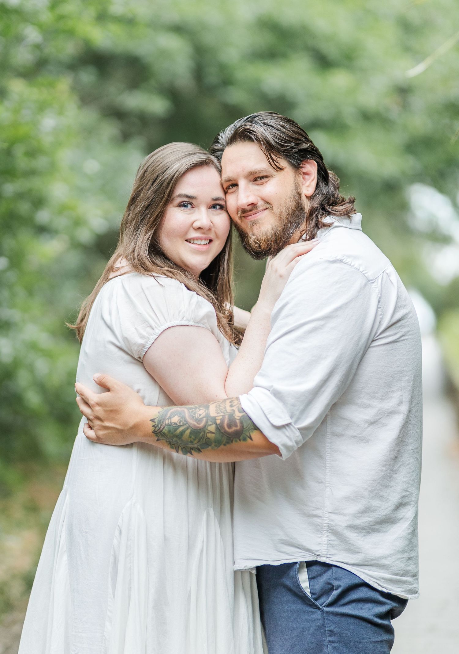 A couple embraces outdoors with green foliage in the background.