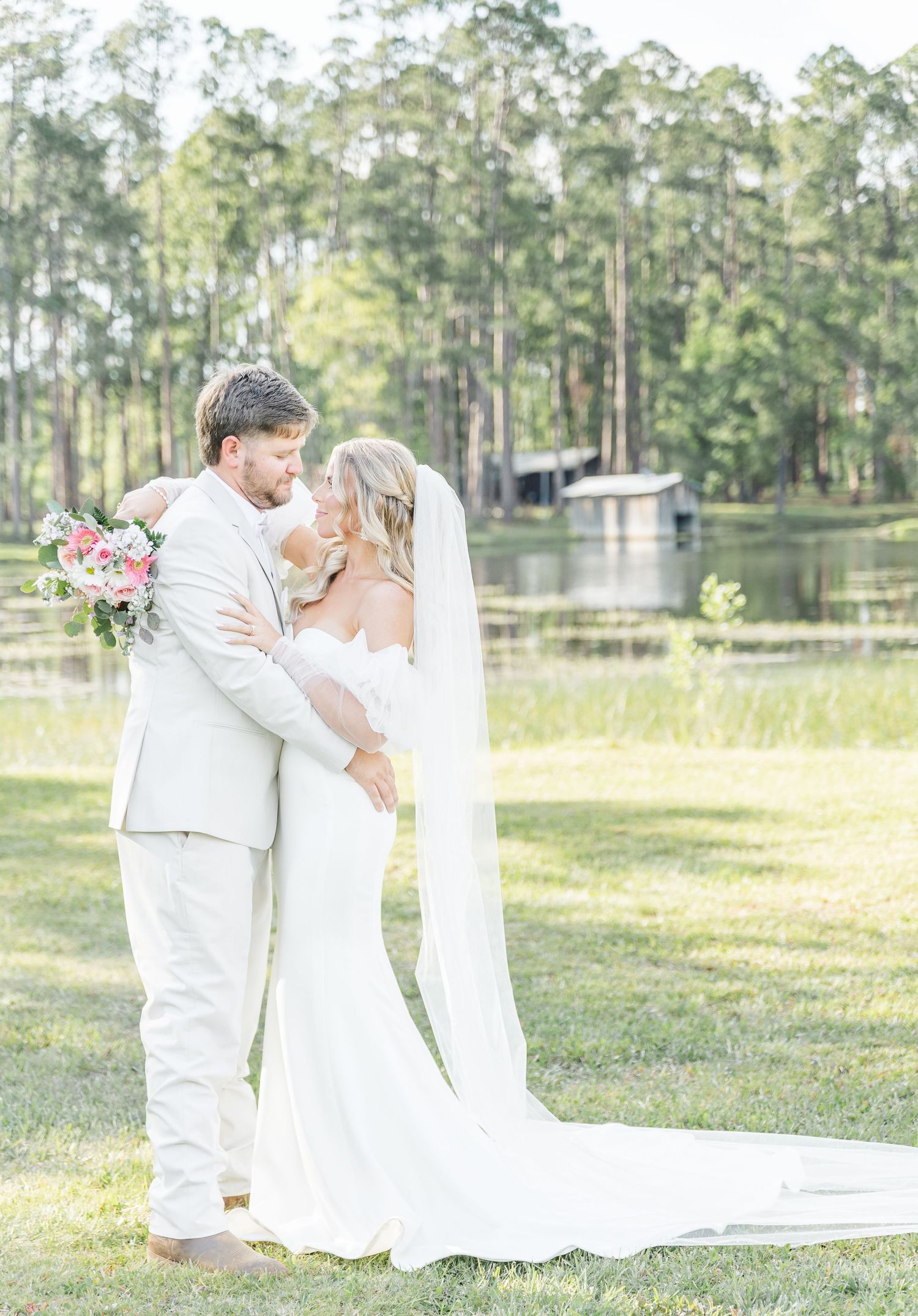 A romantic lakeside wedding photo with a long flowing veil and pine trees in the background.