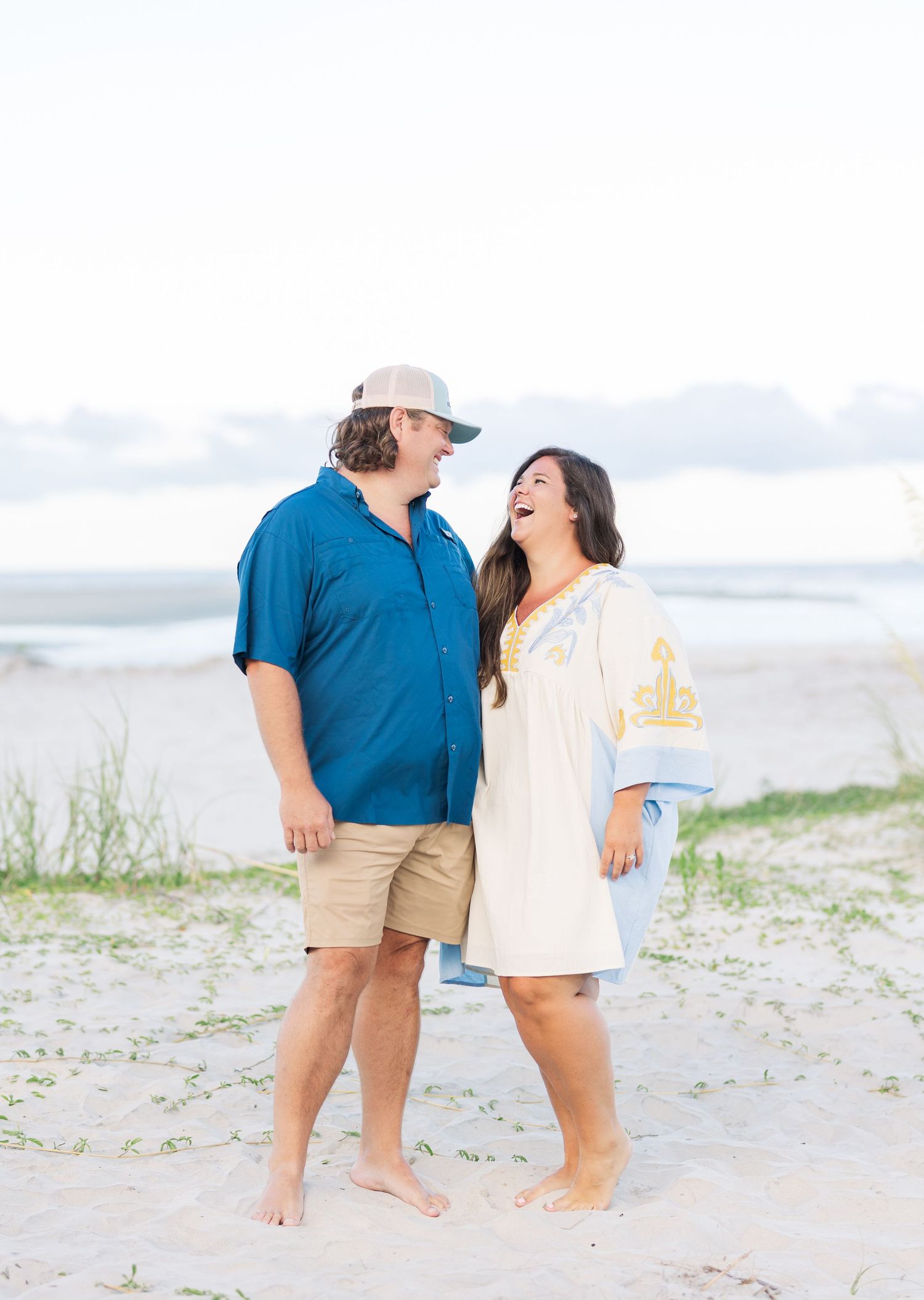 A couple shares a joyful moment together while standing barefoot on a beach.