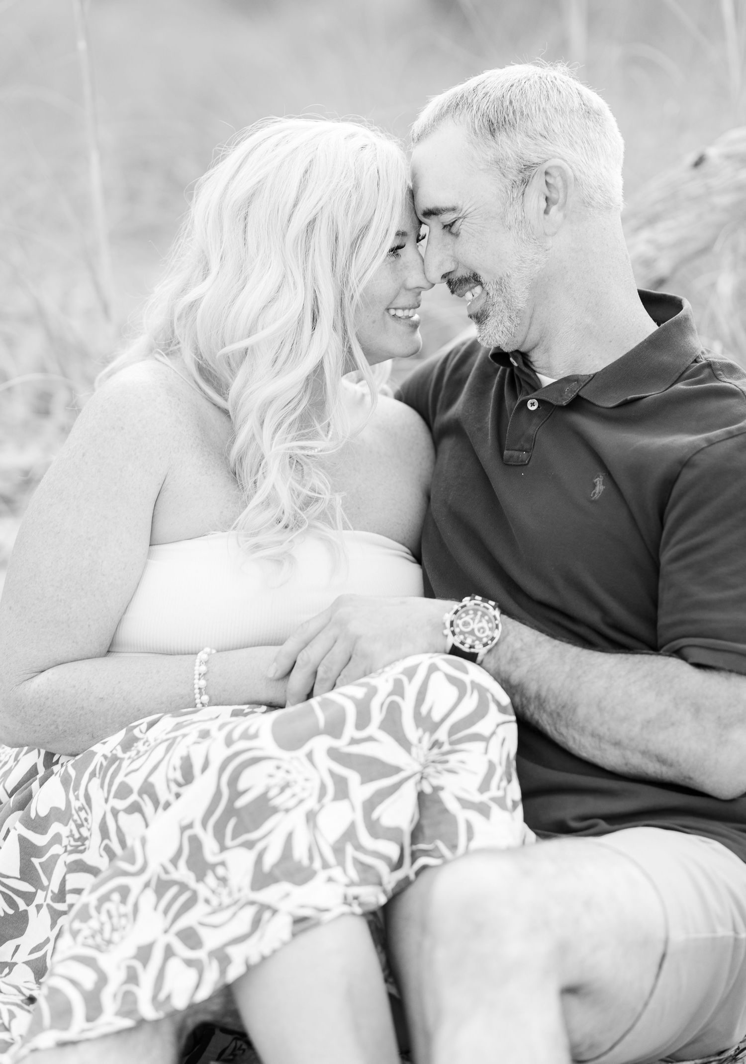 A black and white romantic portrait captures a couple sharing a tender moment while sitting outdoors.