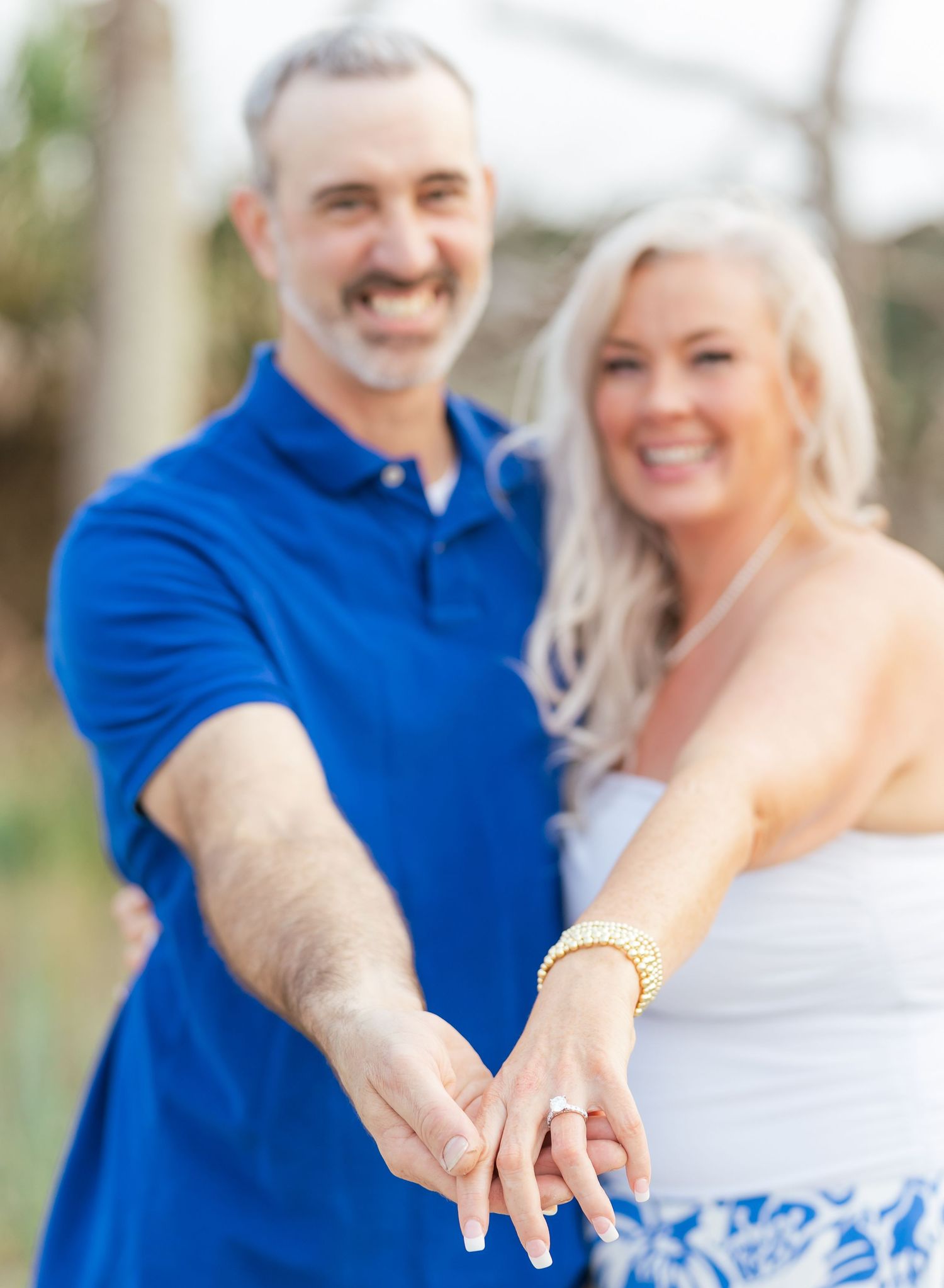 A newly engaged couple shows off the ring in a close-up beach photo.