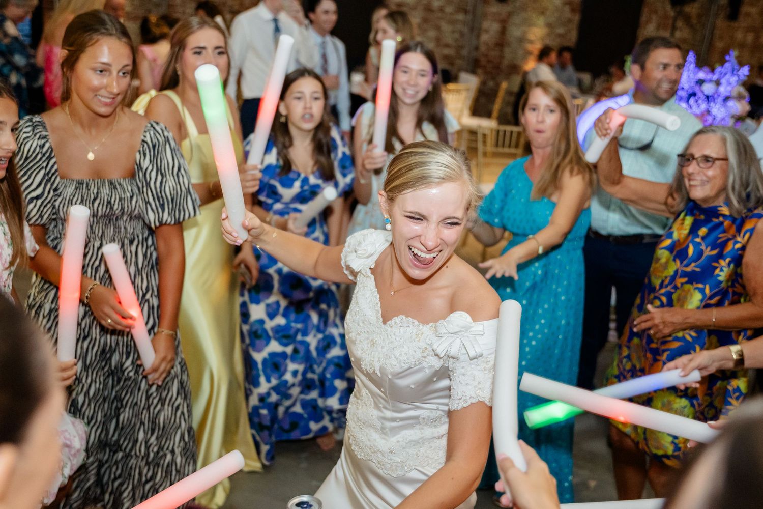 Celebration attendees dance with glowing neon batons in a brick-walled venue.