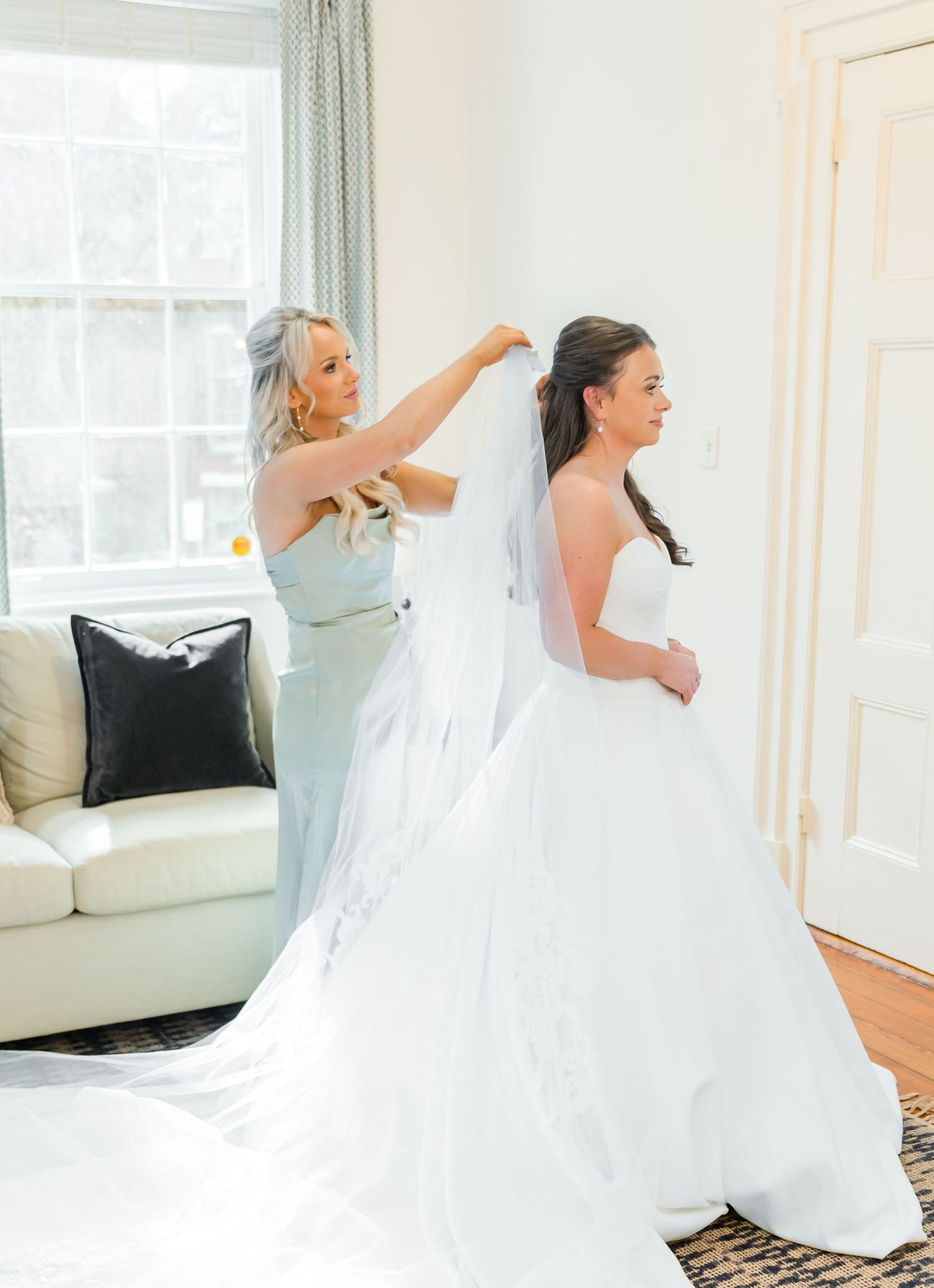 Bride in flowing white wedding dress twirls and dances joyfully in a bright sunlit room with white decor.