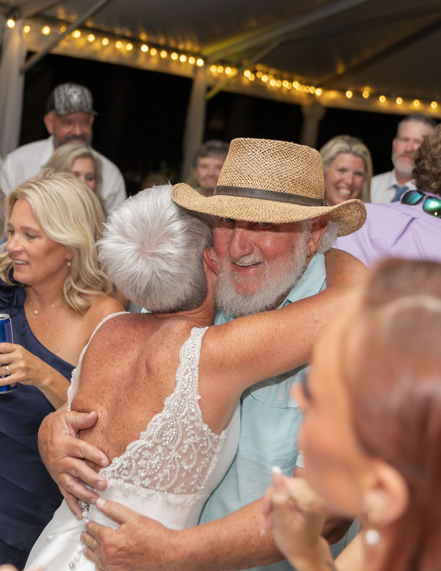 Guests enjoying a lively celebration at a wedding reception with string lights overhead.