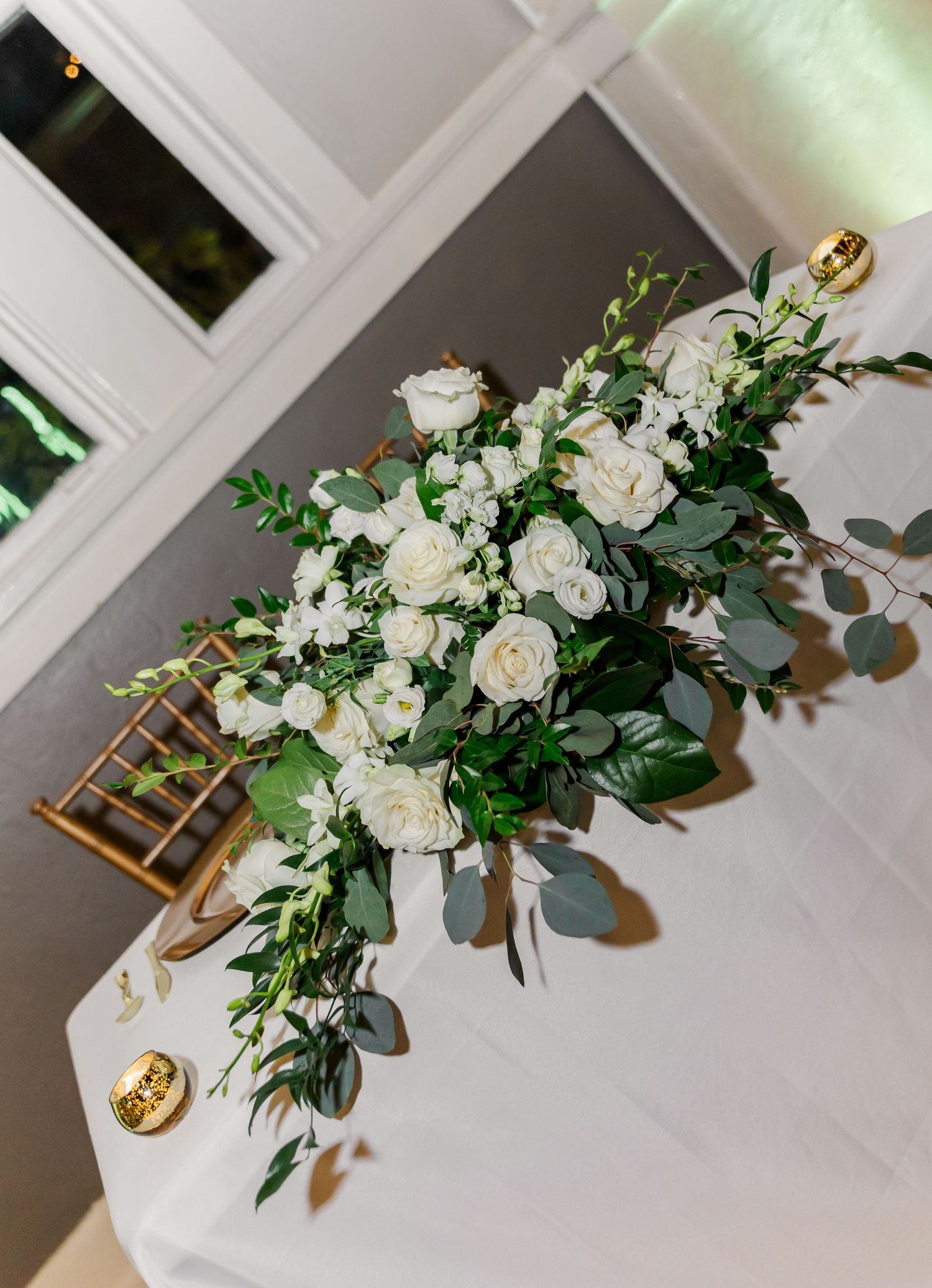 Elegant white floral centerpiece with roses and greenery on a white tablecloth.