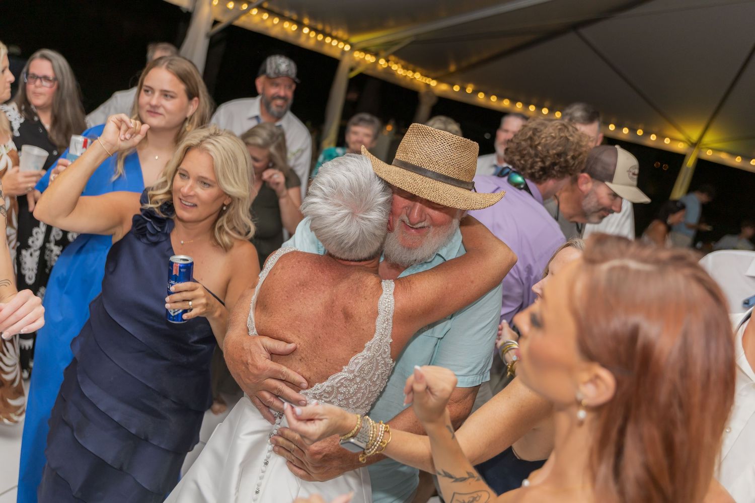 Couples dancing together at a lively party or celebration with festive lighting in the background.