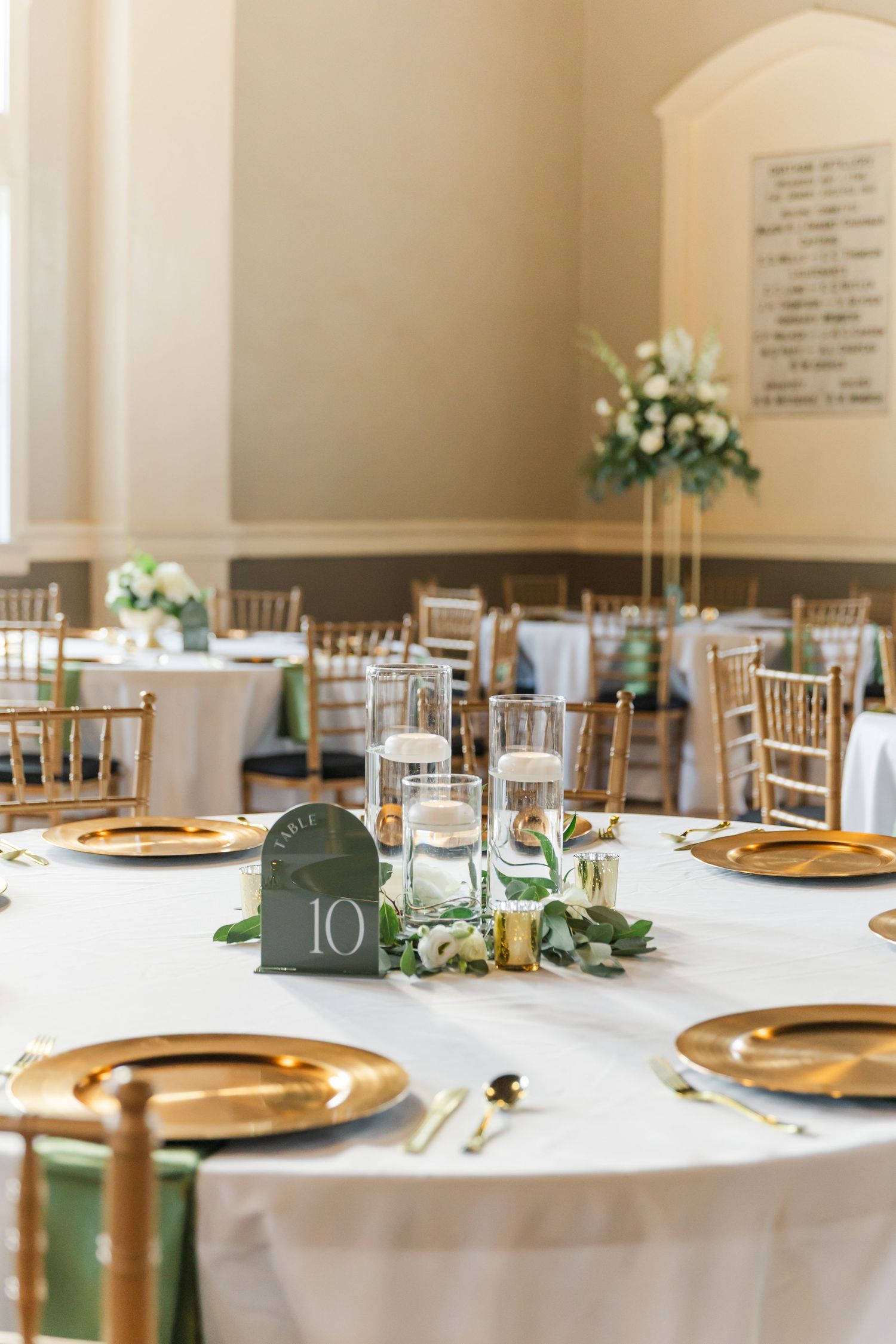 Formal wedding reception venue with white tablecloths, gold chargers, and chiavari chairs.