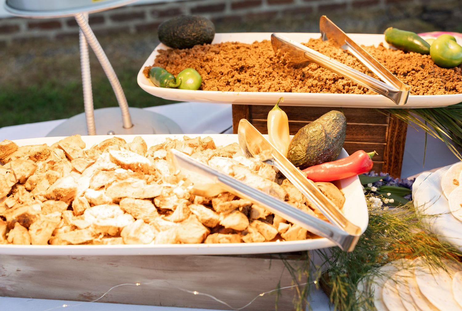 Wedding buffet featuring grilled chicken, seasoned meat, and fresh garnishes in serving trays.
