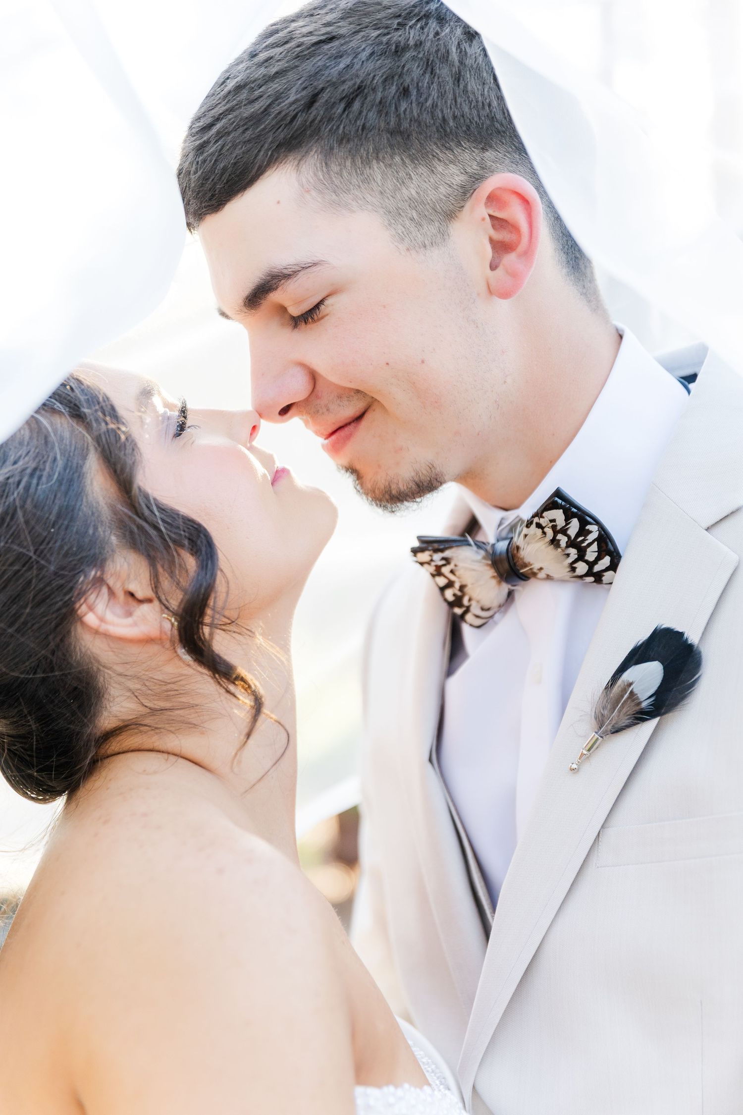 Bride and groom sharing a romantic almost-kiss moment, groom wearing feather bow tie and boutonniere.