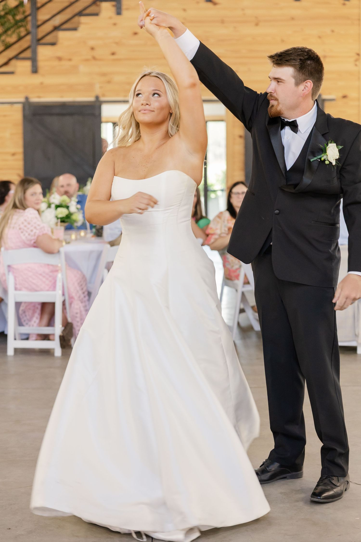 Bride and groom share first dance, groom spinning bride in white strapless ball gown at reception.
