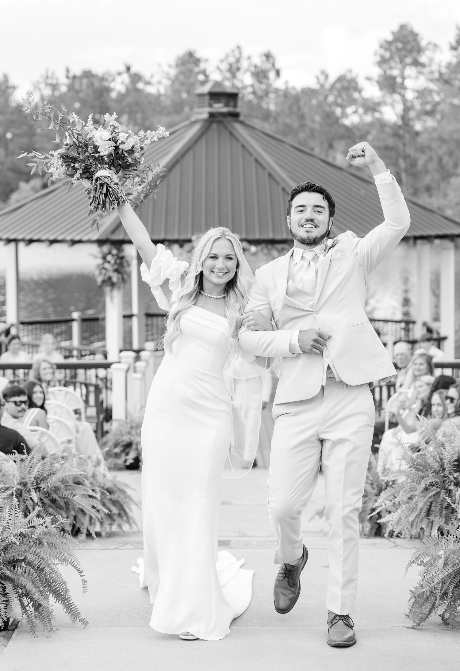 Black and white photo of ecstatic newlyweds celebrating after their outdoor gazebo ceremony.