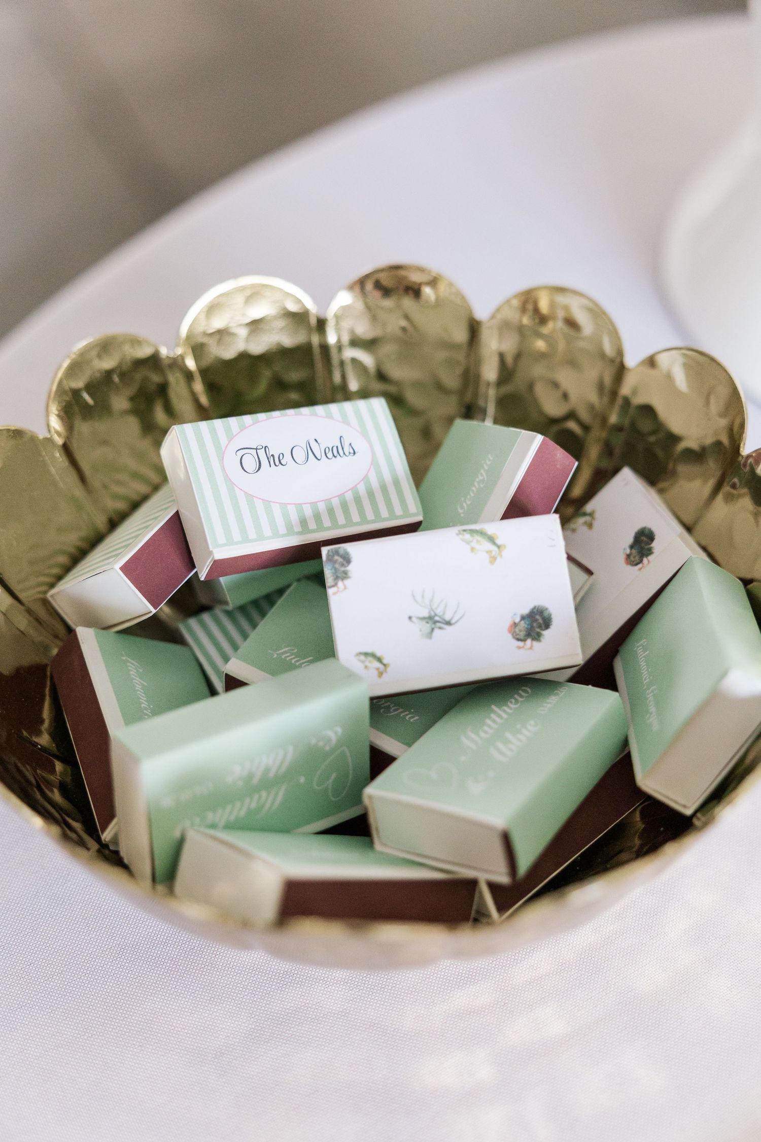 Gold bowl filled with mint green custom wedding favor matchboxes labeled The Neils for an elegant reception.