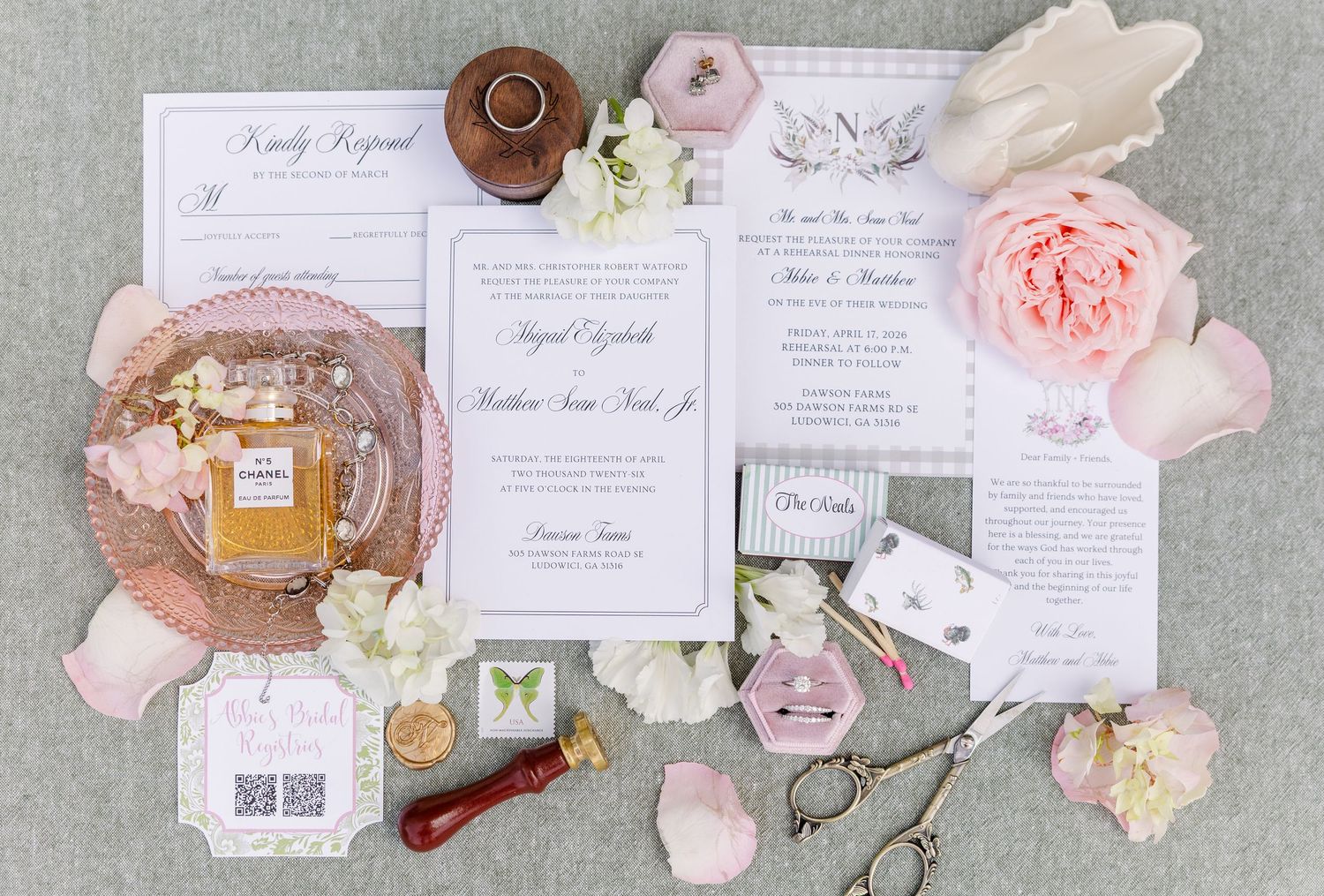 Wedding stationery flat lay featuring invitations, save the dates, perfume, and floral accents.