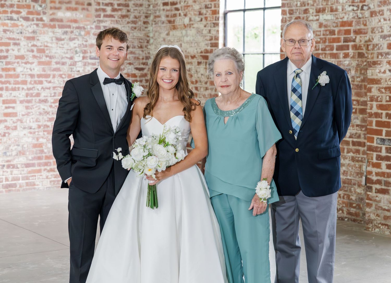 Newlywed couple poses with grandparents in teal and navy at rustic brick wedding venue.