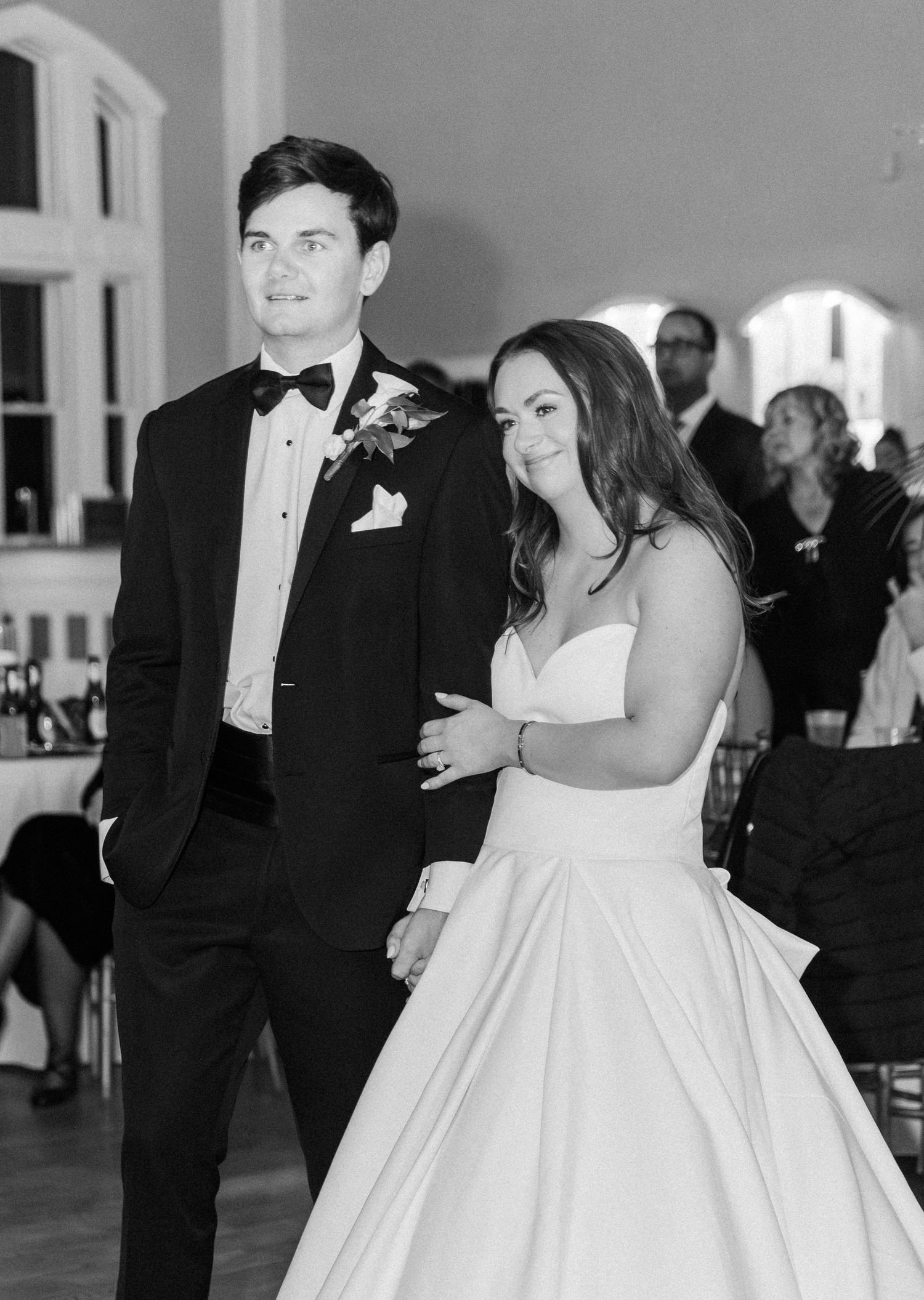 Black and white photo of a bride and groom entering their wedding reception, bride in strapless gown, groom in tuxedo.