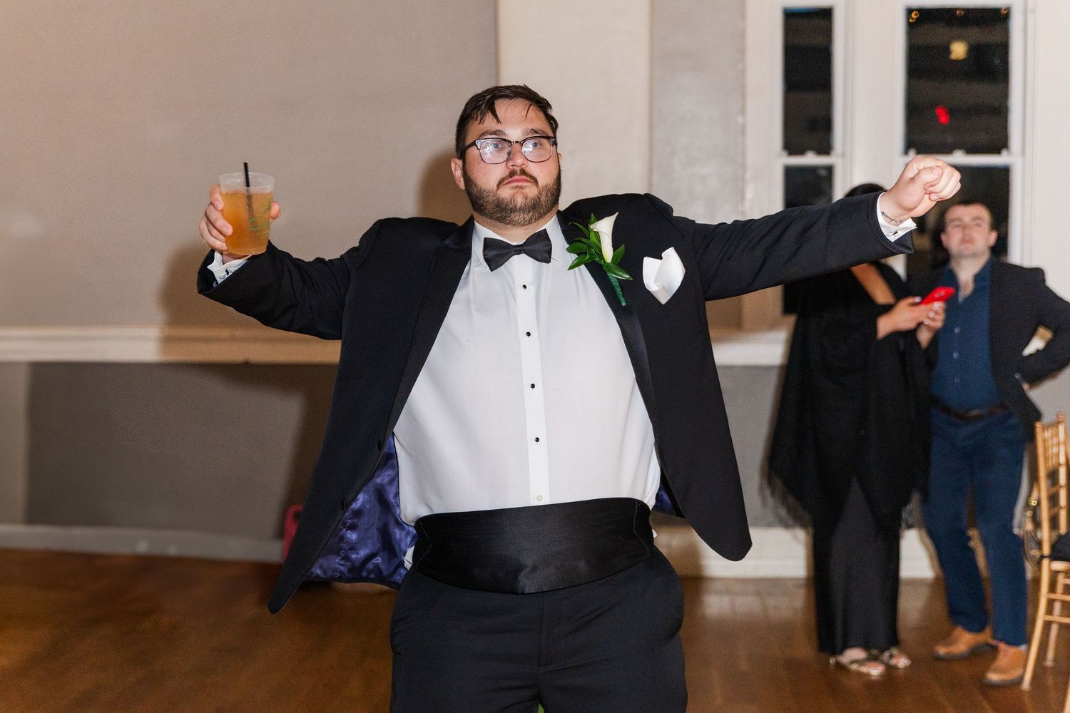 Groomsman in tuxedo with bow tie striking a fun pose on the wedding reception dance floor.