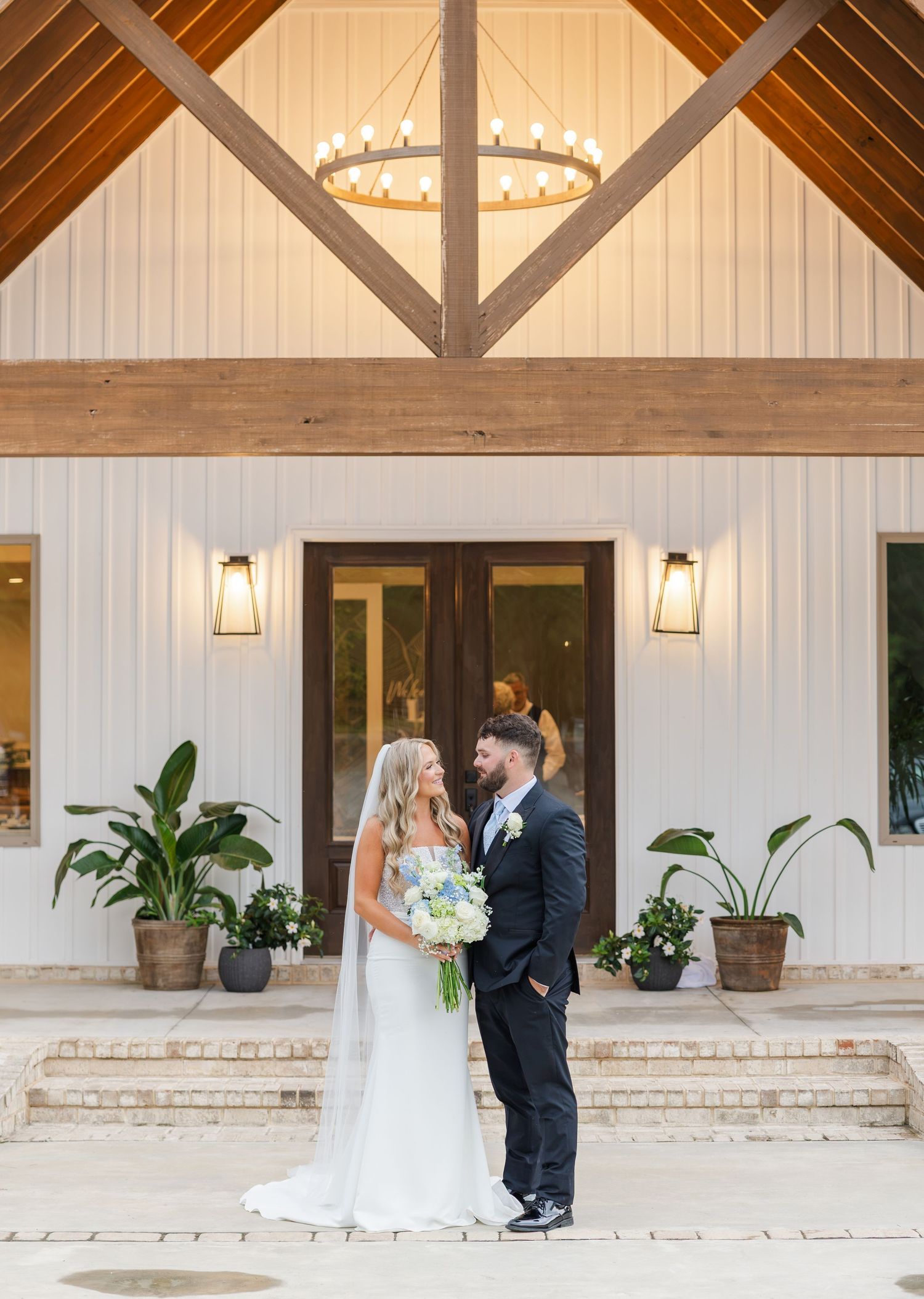 Bride and groom portrait outside white barn wedding venue with wood beam accents.